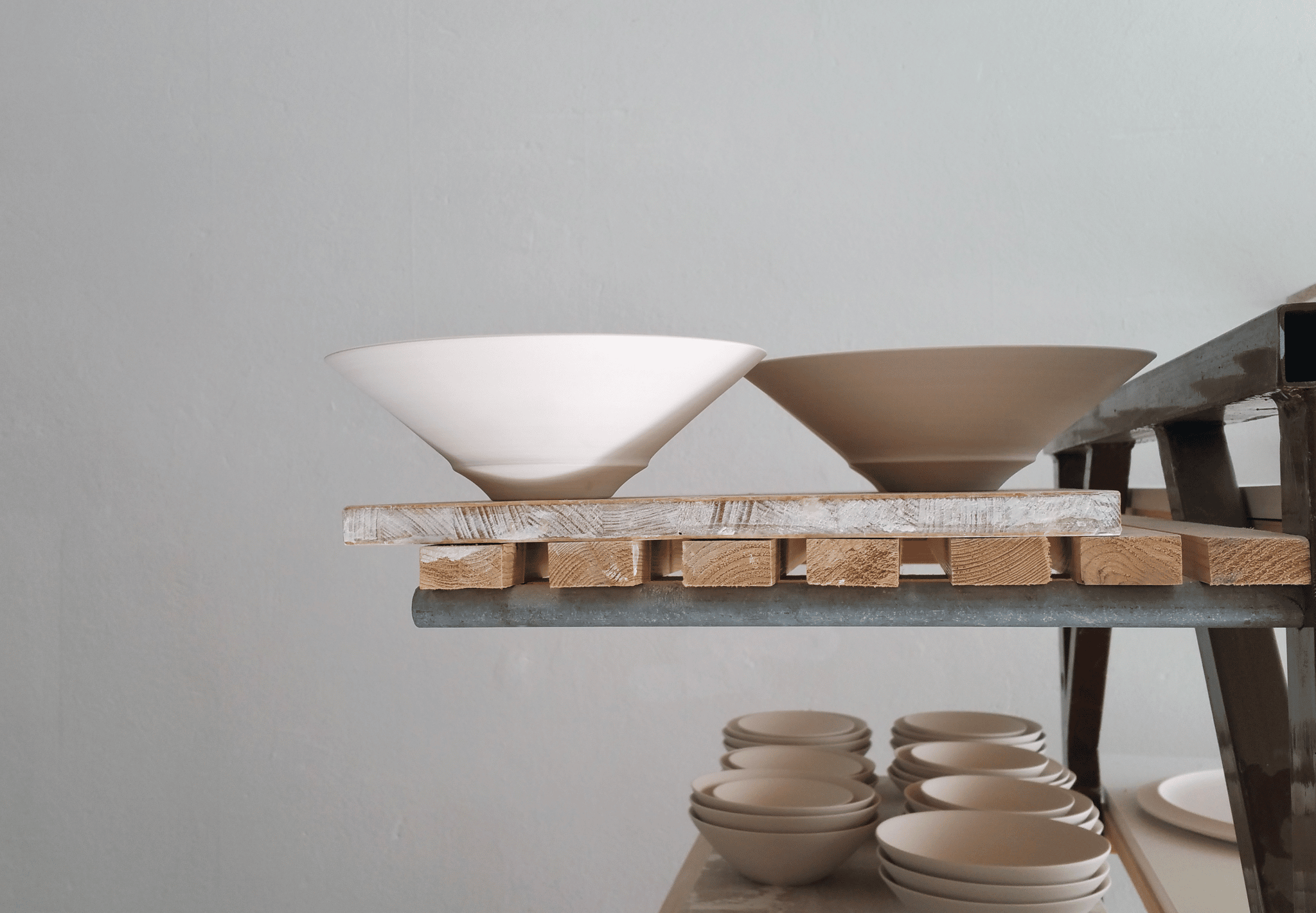 Schlichte, unglasierte Porzellanschalen auf einem Holzregal, im Hintergrund weitere Schalen.