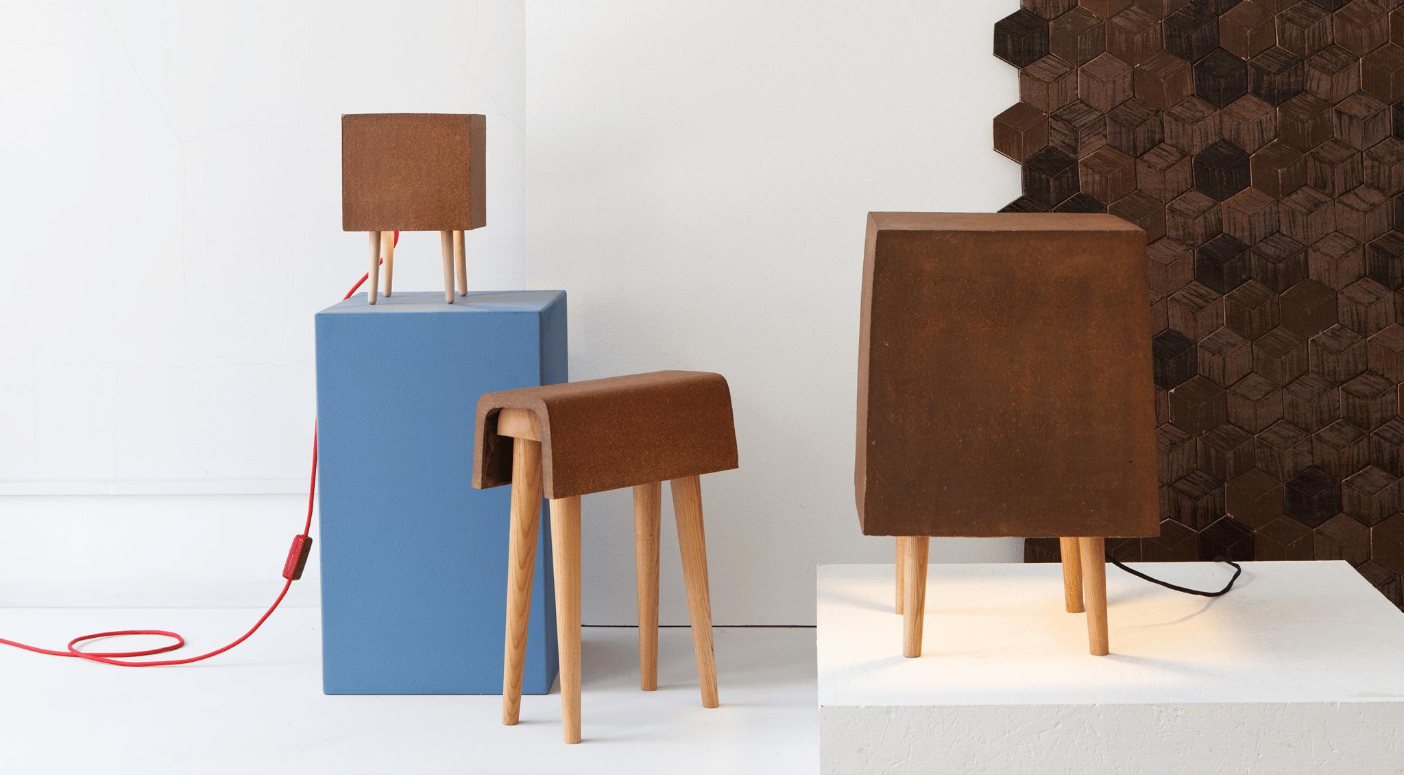 Drei Tischleuchten mit Holzbeinen, eine auf einem blauen und eine auf einem weißen Podest, im modernen Innenraum.