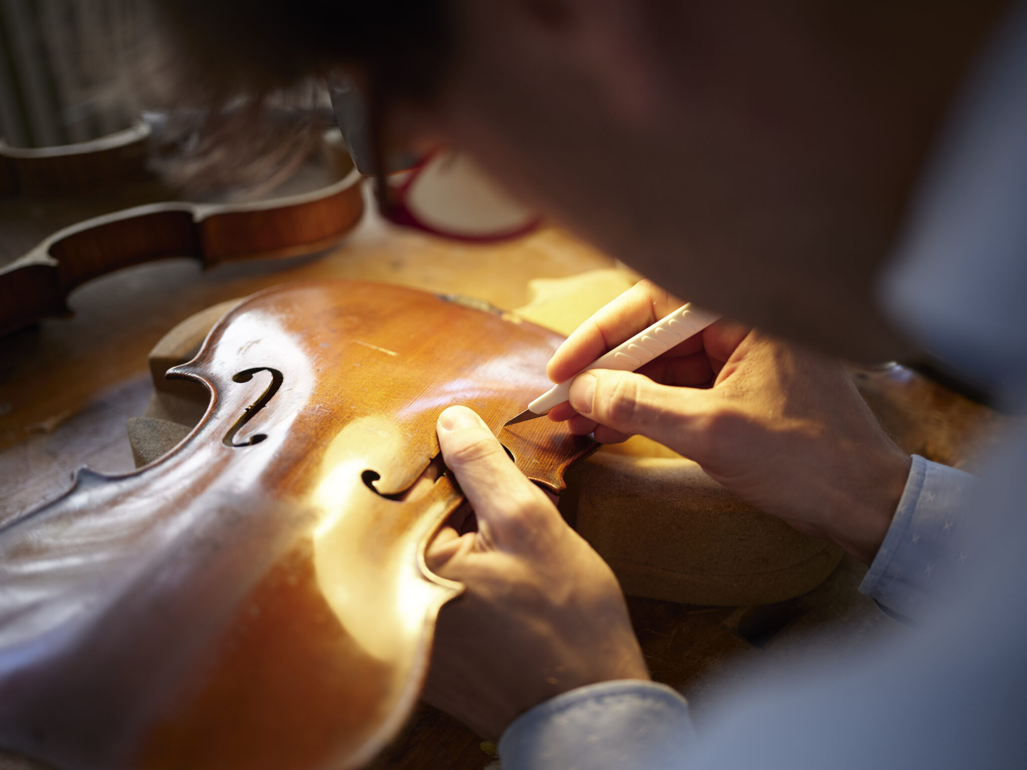 Detailaufnahme eines Geigenbauers, der sorgfältig an der F-Löcher einer Violine arbeitet.