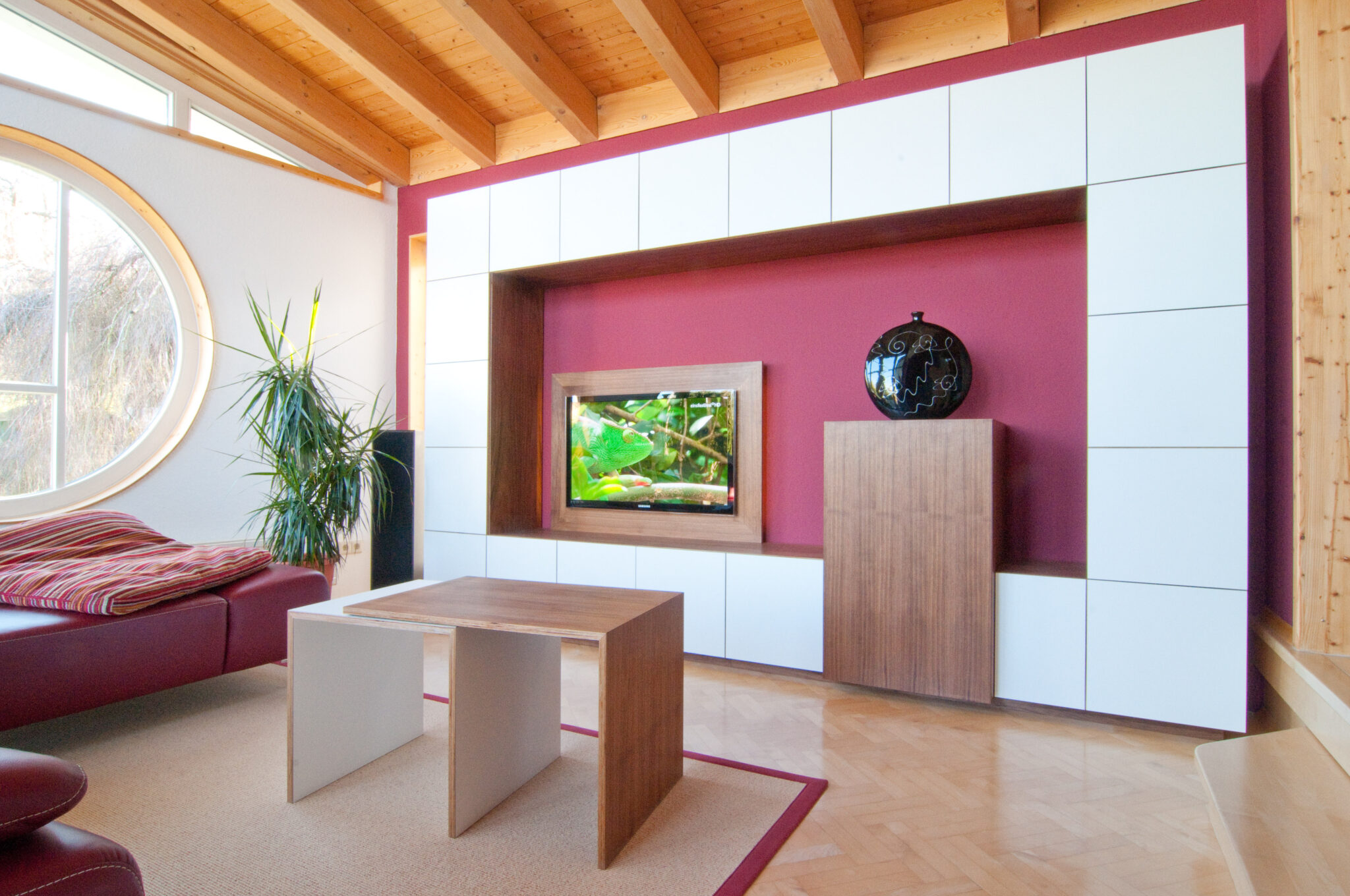 Moderner Wohnraum mit einem Fernsehschrank aus Nussbaum, weißen Wandschränken und einem runden Fenster.