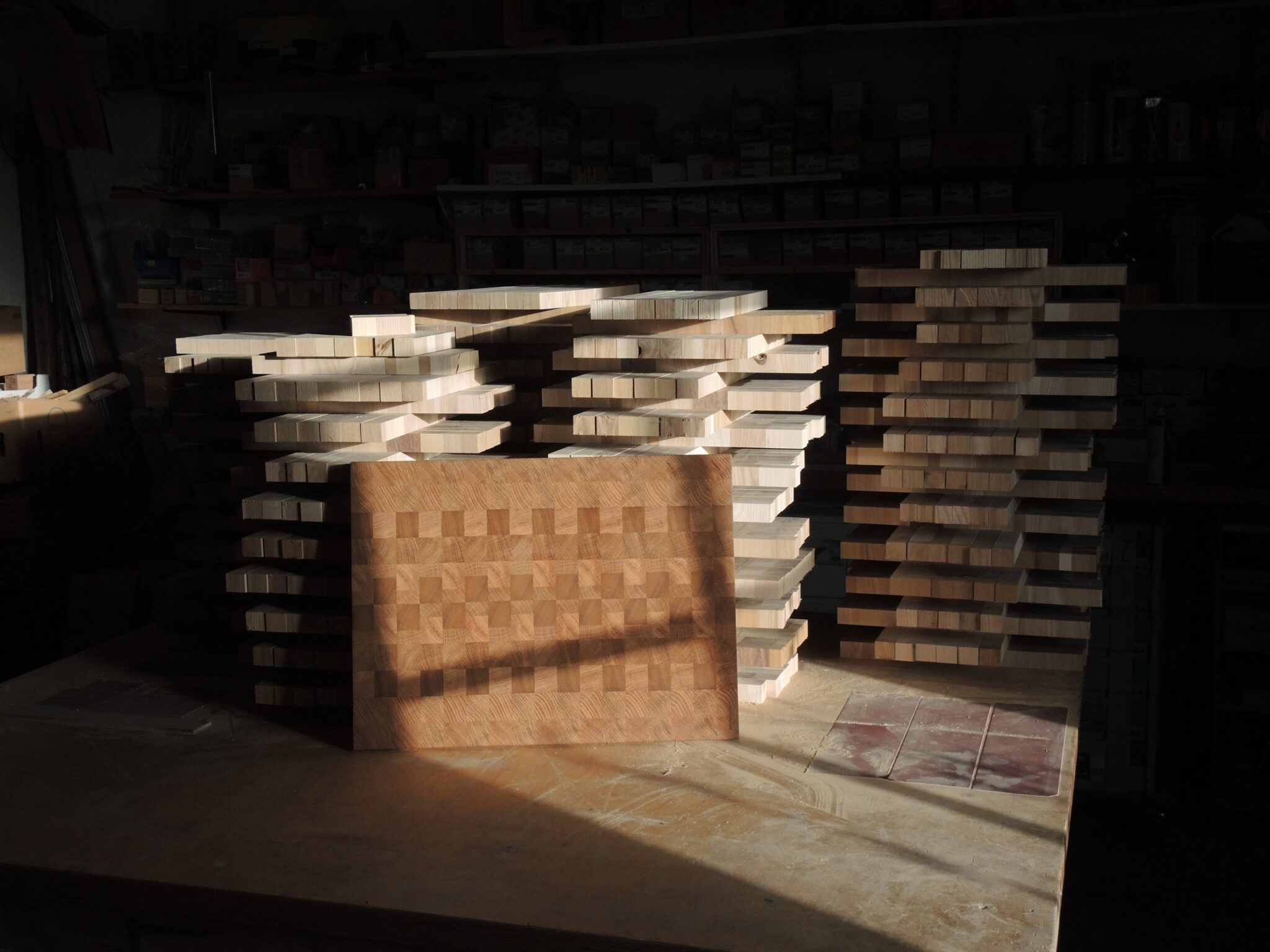 werkstatt3 - Deutsche Manufakturenstrasse Holzwerkstatt mit gestapelten Holzstücken und einem großen Holzbrett auf einem Tisch.