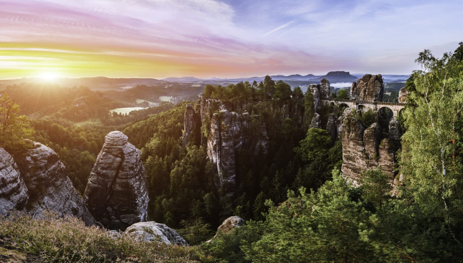 - Deutsche Manufakturenstrasse Sonnenaufgang über der Bastei mit Blick auf die Basteibrücke und Felsformationen im Gegenlicht.