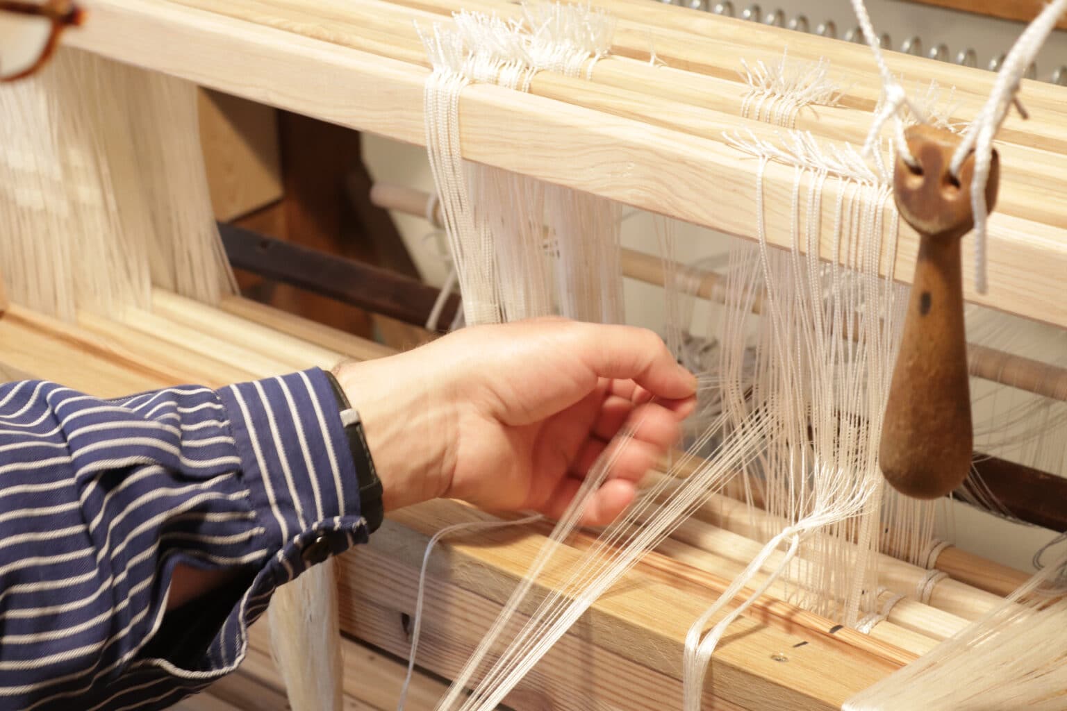 ETAK-Weberei-C-Hannes-Feine-Manufaktur - Deutsche Manufakturenstrasse Detailaufnahme einer Hand, die an einem Webstuhl mit weißen Fäden arbeitet, im Kontext der Europäischen Tage des Kunsth...