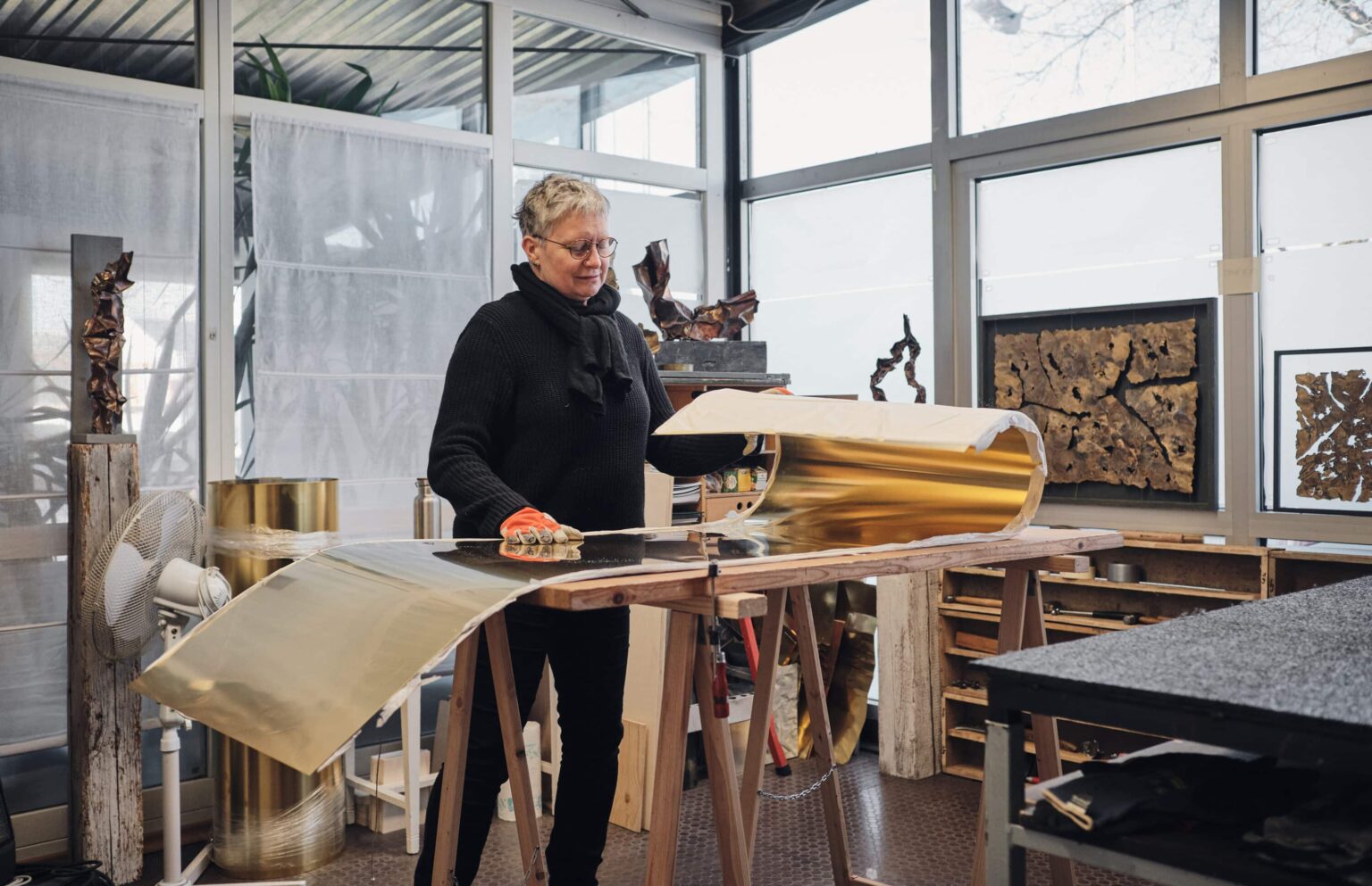 Manuela Geugelin arbeitet in ihrem Atelier mit goldfarbenem Metall auf einem Tisch.