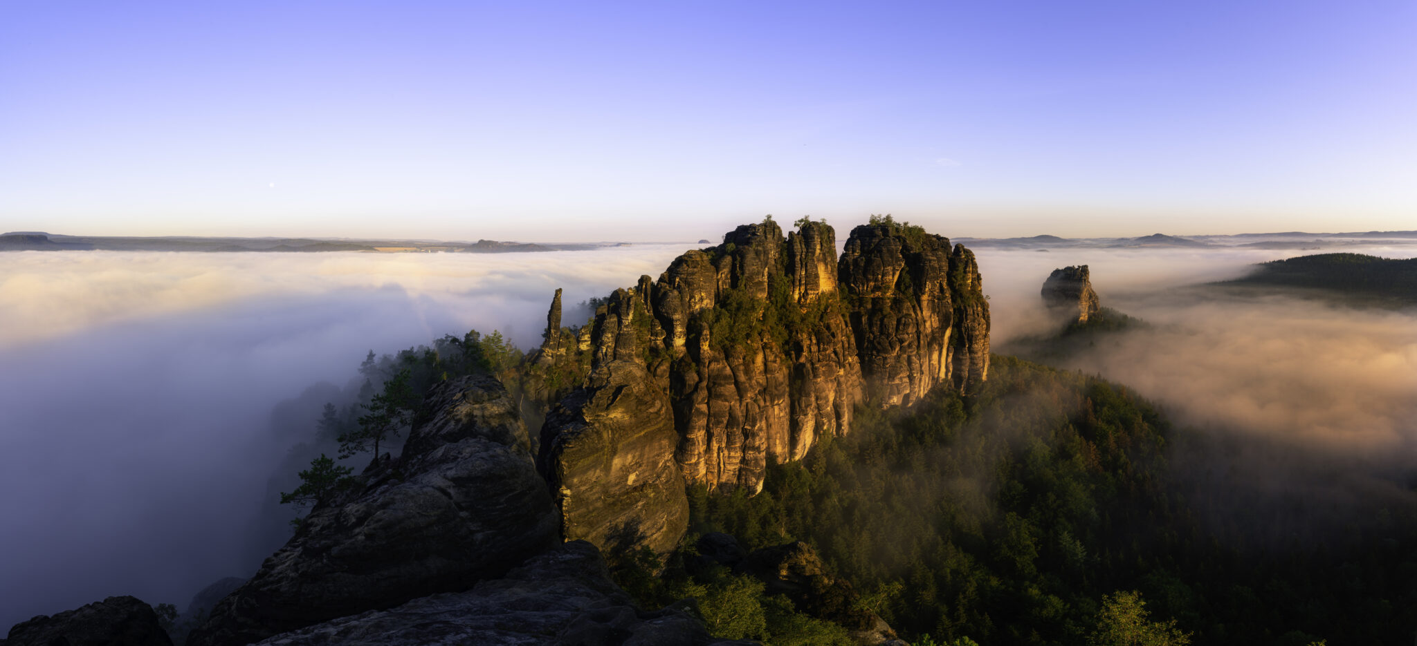 Schrammsteinaussicht in der Sächsischen Schweiz, umgeben von Nebel und Sonnenlicht, mit markanten Felsen und Bäumen.