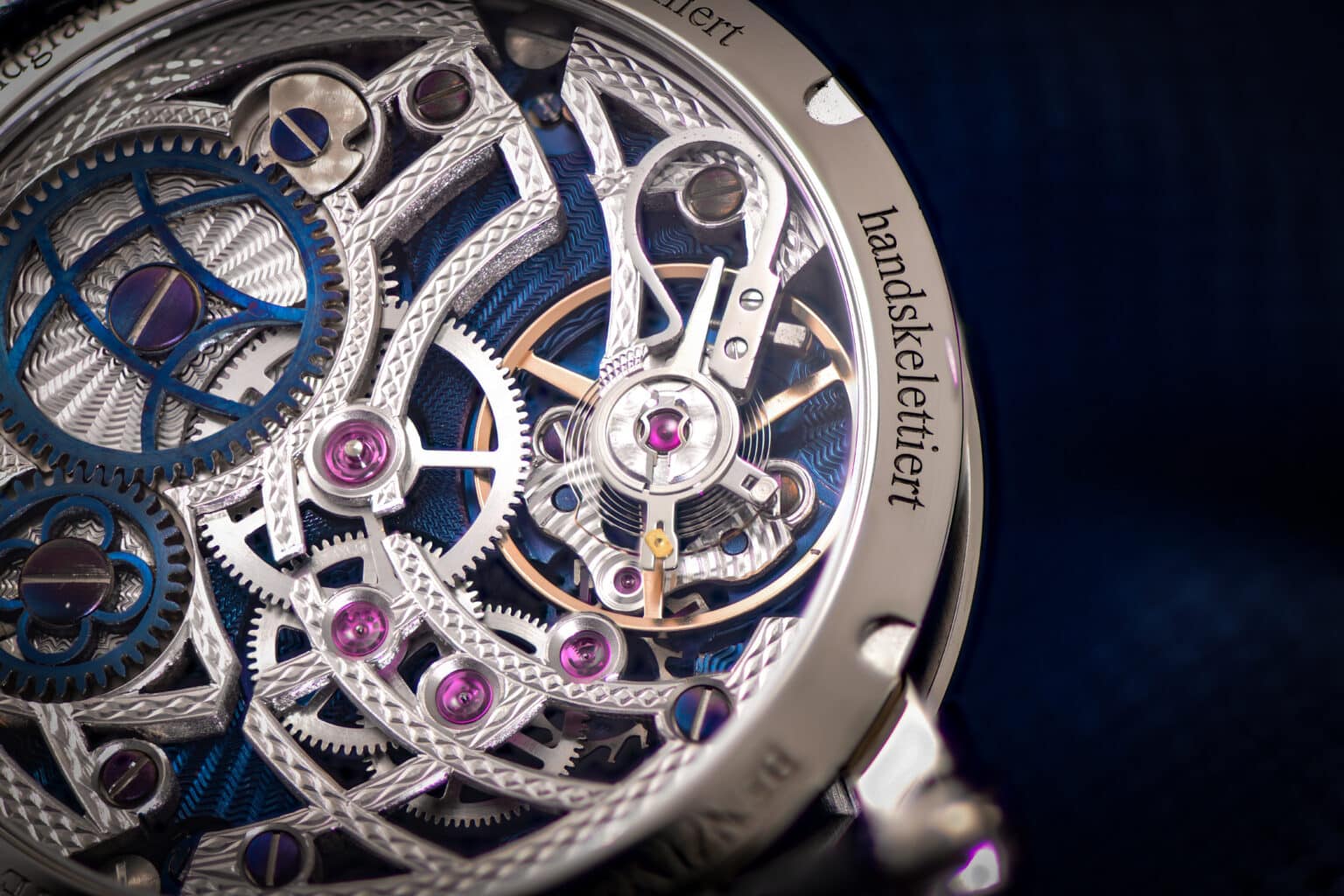 benzinger-blue-ray-7 - Deutsche Manufakturenstrasse Detailansicht einer mechanischen Uhr mit sichtbarem Uhrwerk, blauen und silbernen Elementen sowie pinken Rubinen.