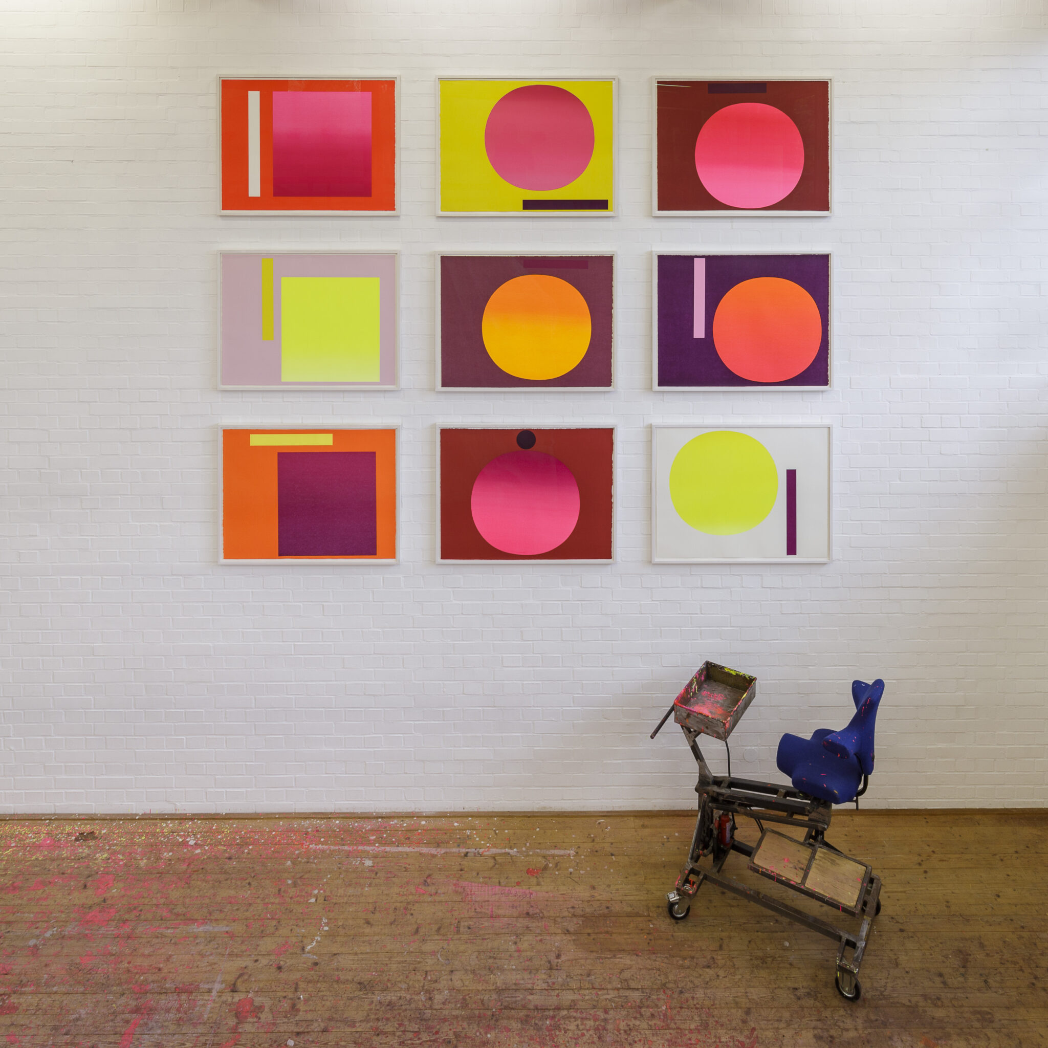 2020_Raumaufnahme_Archiv_Geiger_Foto_Marian_Wilhelm_Muenchen - Deutsche Manufakturenstrasse Neun geometrische Kunstwerke in leuchtenden Farben an einer weißen Wand, Teil des Archivs Geiger.