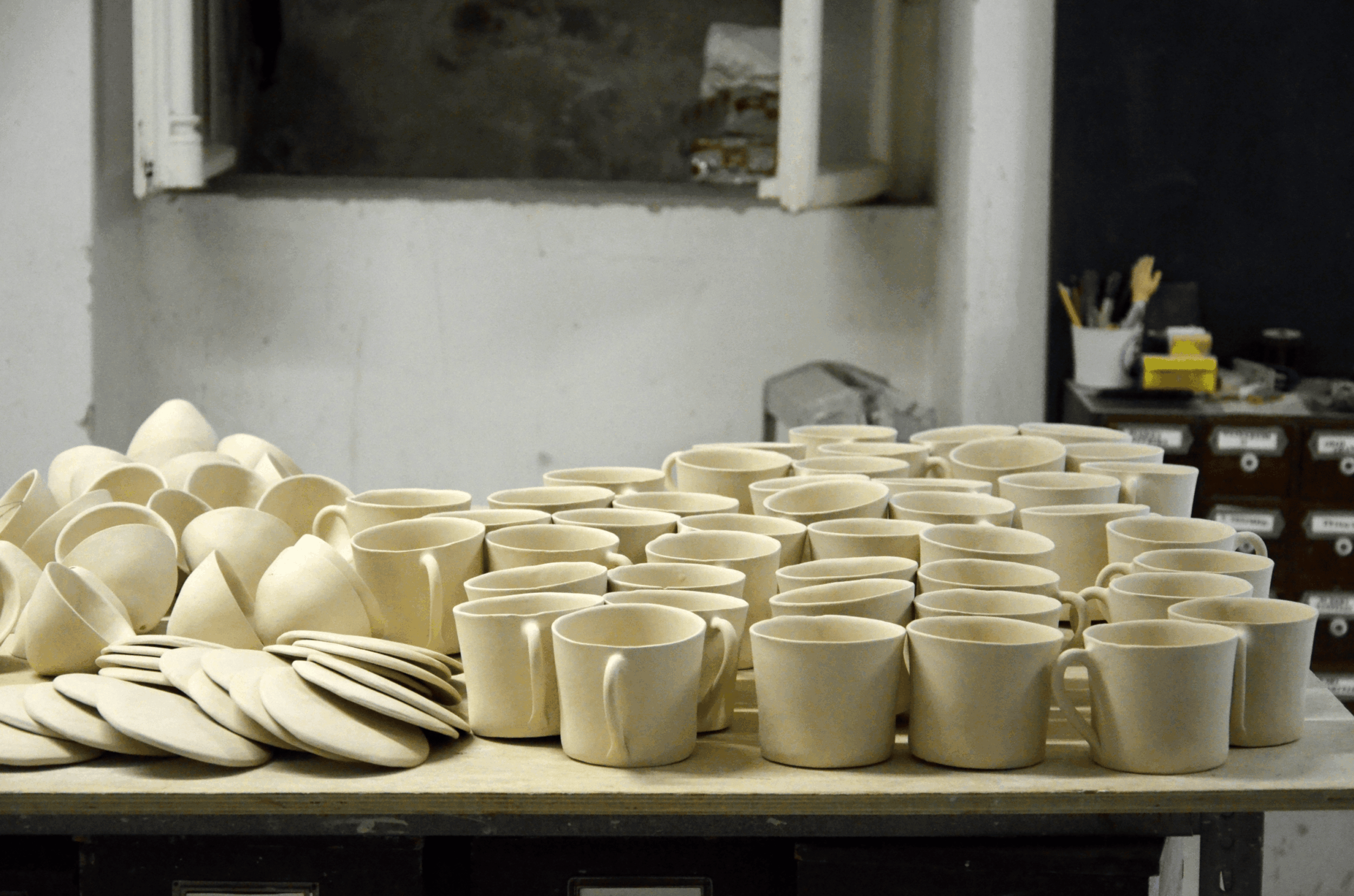 Schruehware_1 - Deutsche Manufakturenstrasse Töpferwaren aus unglasiertem Ton, darunter Becher und Teller, auf einem Tisch in einer Werkstatt.