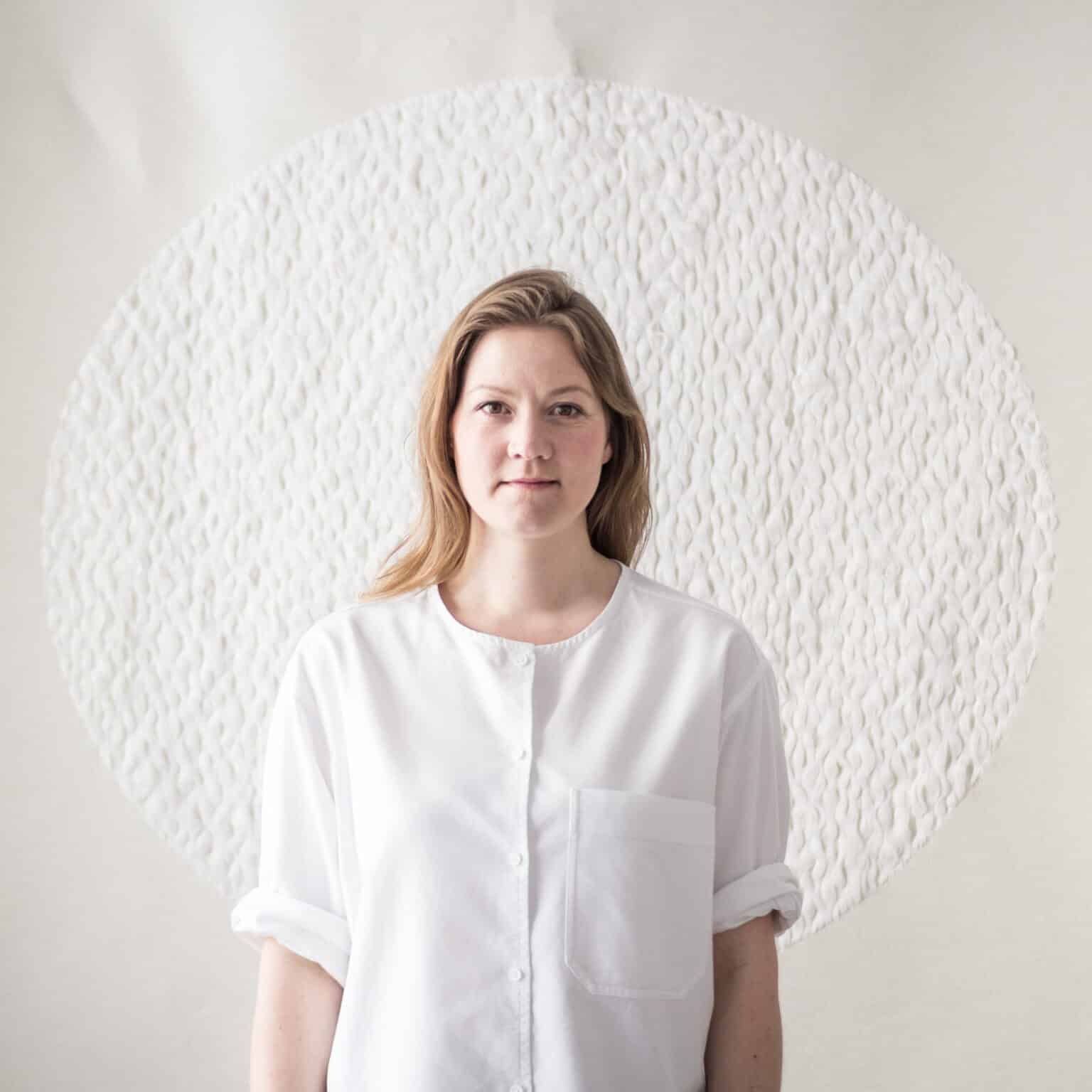 20172505_sRGB_1 - Deutsche Manufakturenstrasse Frau mit langen Haaren in weißem Hemd vor strukturiertem, hellen Hintergrund. Kontext: Die Zukunft des Webens.