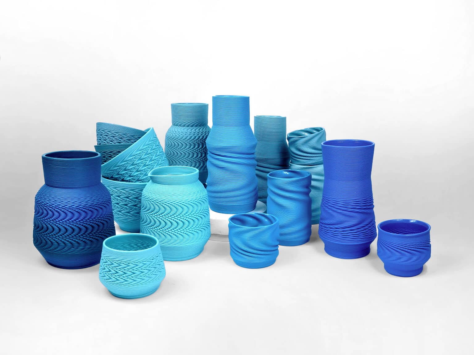 05_porcelain series_breeze_deepblue_supersonic_overview_05 - Deutsche Manufakturenstrasse Verschiedene Vasen in Blau- und Türkistönen, mit unterschiedlichen Texturen und Formen, auf einem hellen Hintergrund.