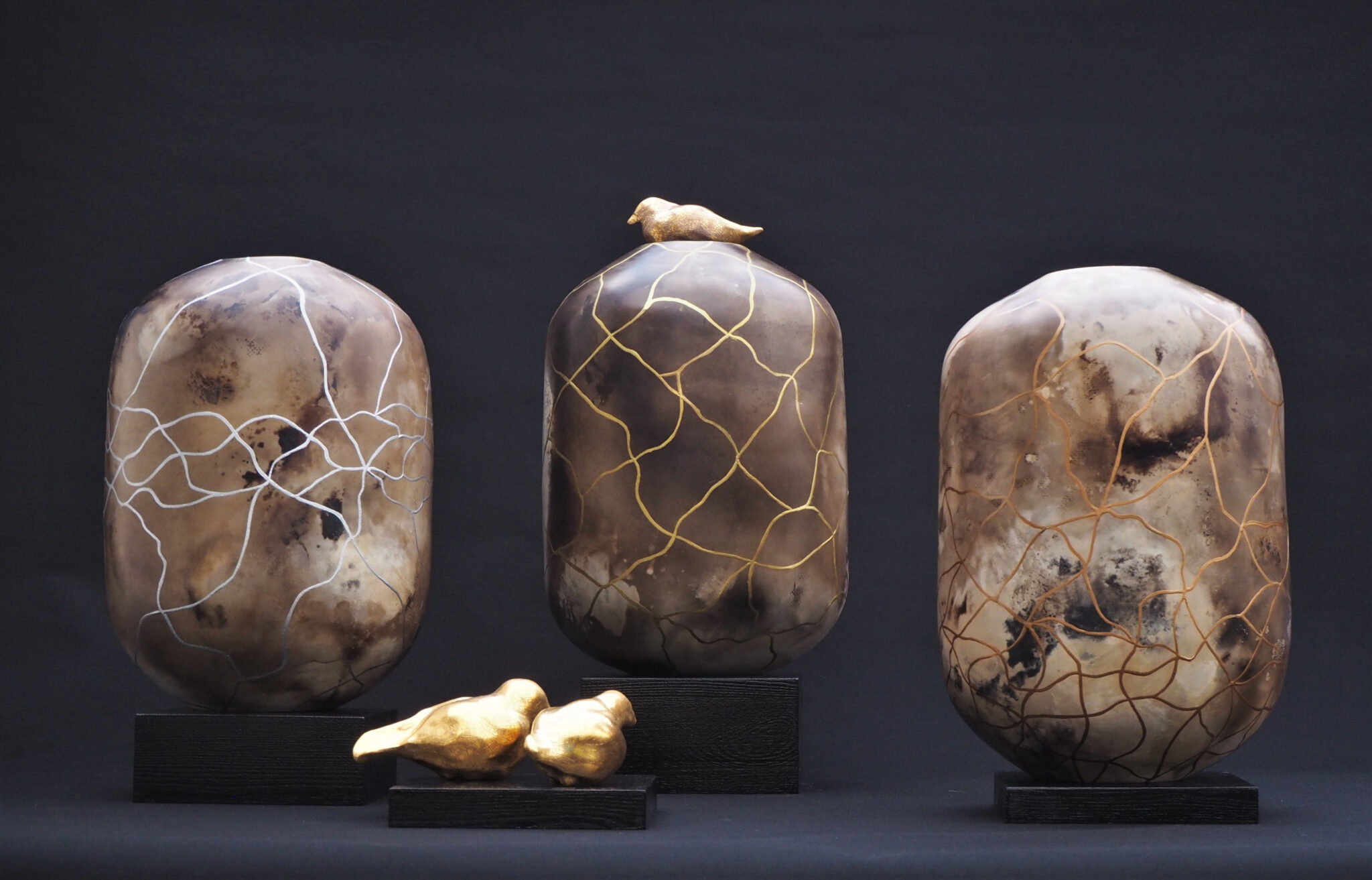 - Deutsche Manufakturenstrasse Drei keramische Skulpturen in erdigen Tönen mit goldenen und weißen Verzierungen, begleitet von zwei kleinen Vögeln.