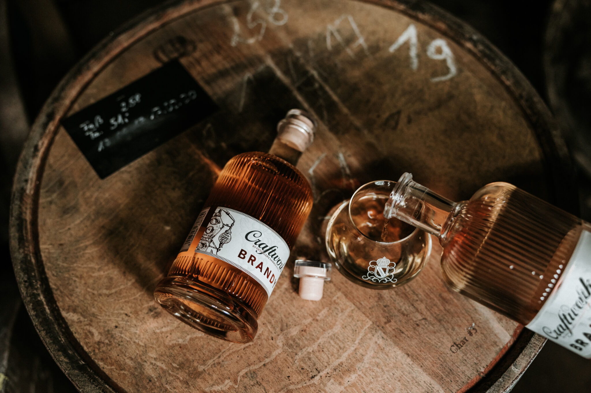 - Deutsche Manufakturenstrasse Flasche Craftwork Brandy und Gläser auf einem Holzfass, umgeben von einer Tafel mit Notizen.