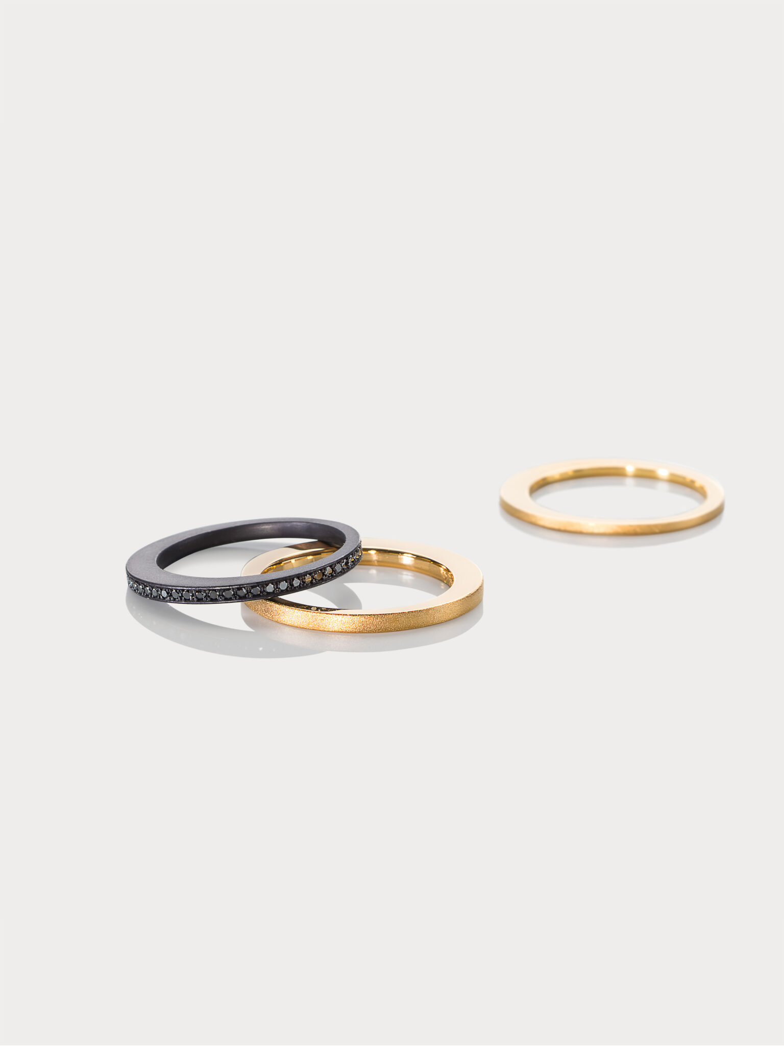 Drei Ringe aus dem Johanna Otto Schmuckdesign: ein schwarzer Ring mit Steinen, zwei goldene Ringe, einer mattiert, einer g...