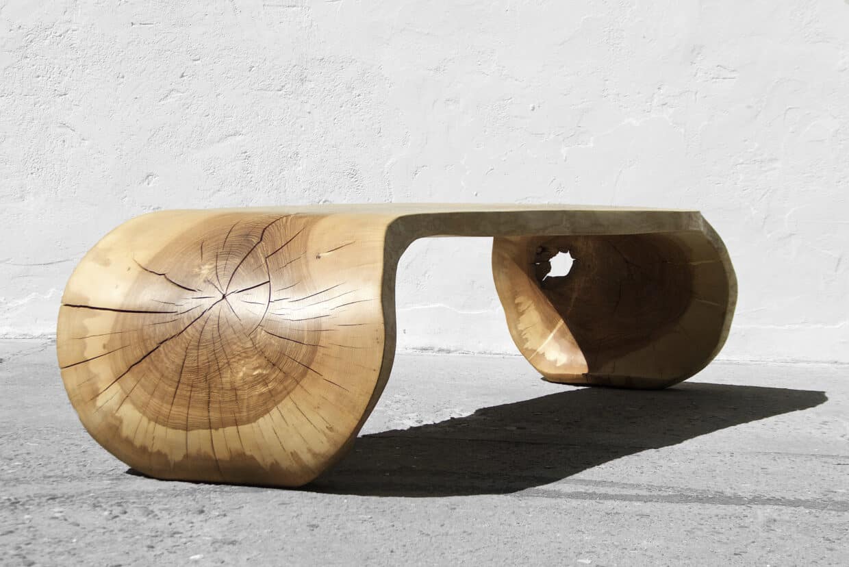 Holztisch mit geschwungenen Beinen aus massivem Holz, auf grauem Untergrund vor einer weißen Wand.