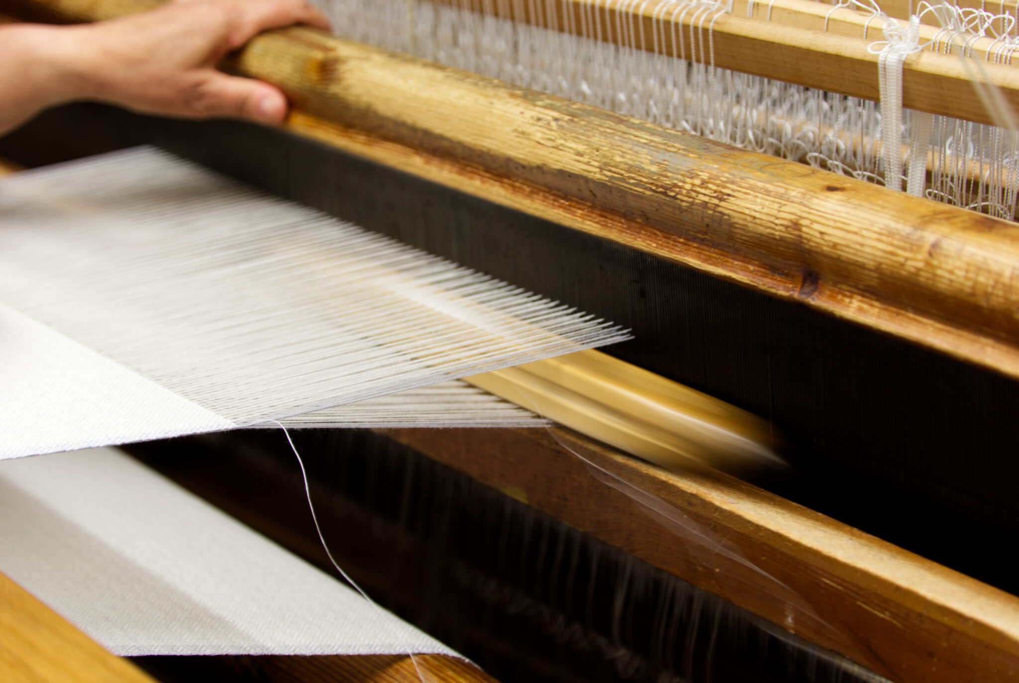 - Deutsche Manufakturenstrasse Hand bedient einen Webstuhl, während Fäden durch einen Holzrahmen gezogen werden.