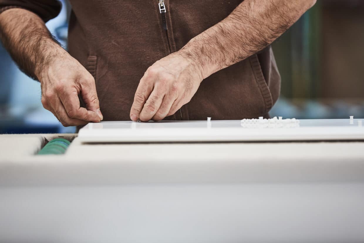 Hände eines Arbeiters, die präzise Teile auf einer weißen Oberfläche anordnen, in einer Werkstatt von Interlübke.