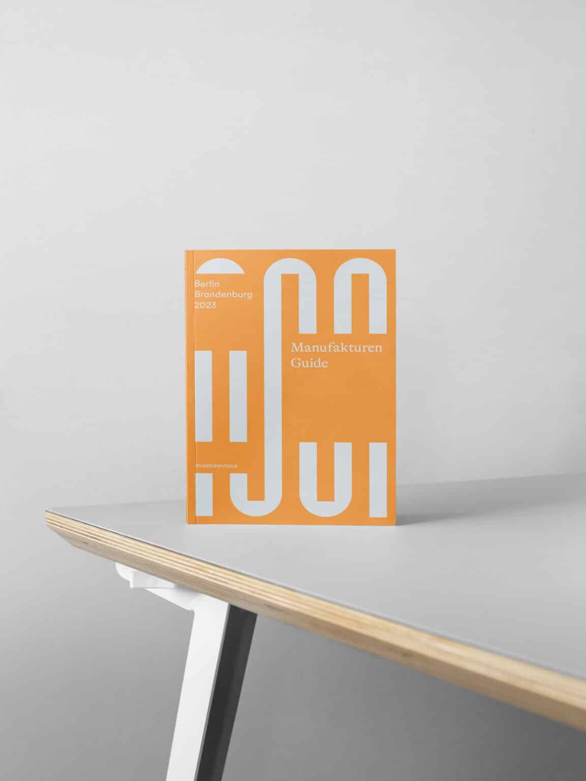 Orangefarbenes Buchcover mit dem Titel "Manufakturen Guide" und dem Untertitel "Berlin Brandenburg 2023" auf einem Tisch.