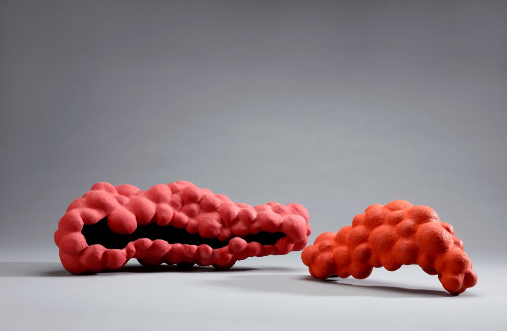 02A7578 - Deutsche Manufakturenstrasse Zwei organisch geformte, rot-orange Skulpturen auf grauem Hintergrund, eine größer und eine kleiner.