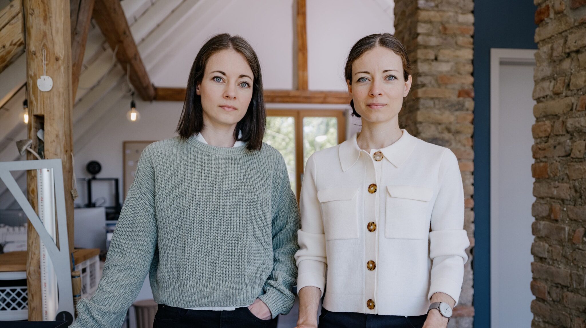 08_burggrafburggraf - Deutsche Manufakturenstrasse Zwei Frauen stehen in einem hellen Raum mit Holzdetails, eine trägt einen grünen Pullover, die andere eine weiße Bluse ...