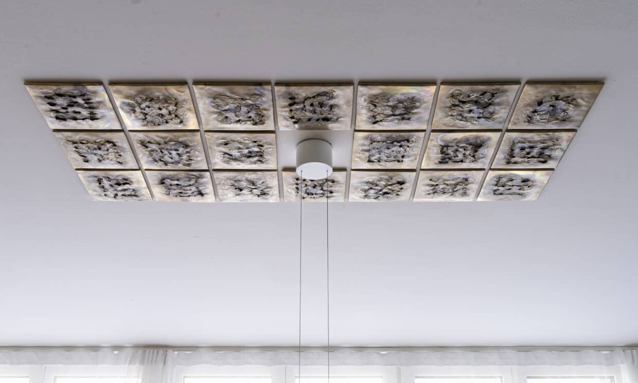 Deckenmosaik Messing 150x66x1cm - Deutsche Manufakturenstrasse Deckenmosaik aus 16 quadratischen Platten in Gold- und Grautönen, mit einer zentralen Lampe.