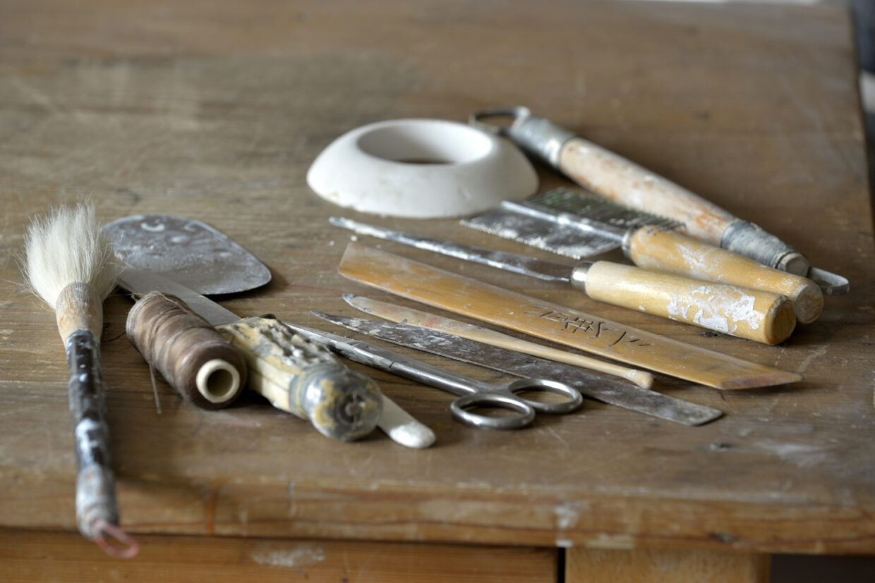 _KD66674 - Deutsche Manufakturenstrasse Werkzeuge und Utensilien auf einem Tisch, darunter Pinsel, Klingen, Schaufel und eine Schüssel.