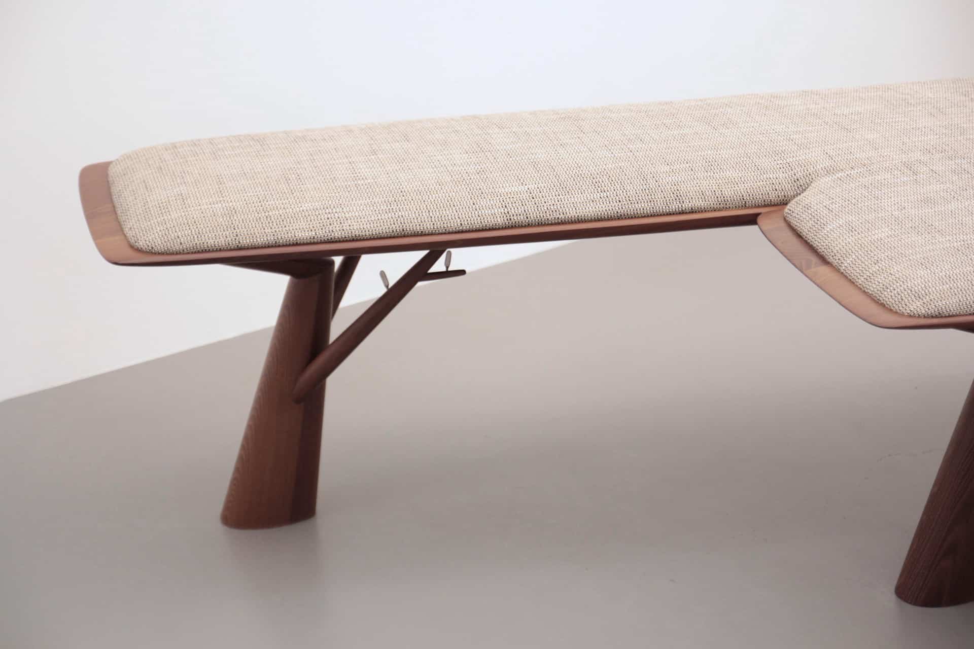 Detail einer Sitzbank mit einem gepolsterten, hellen Sitz und geschwungenen Holzbeinen.