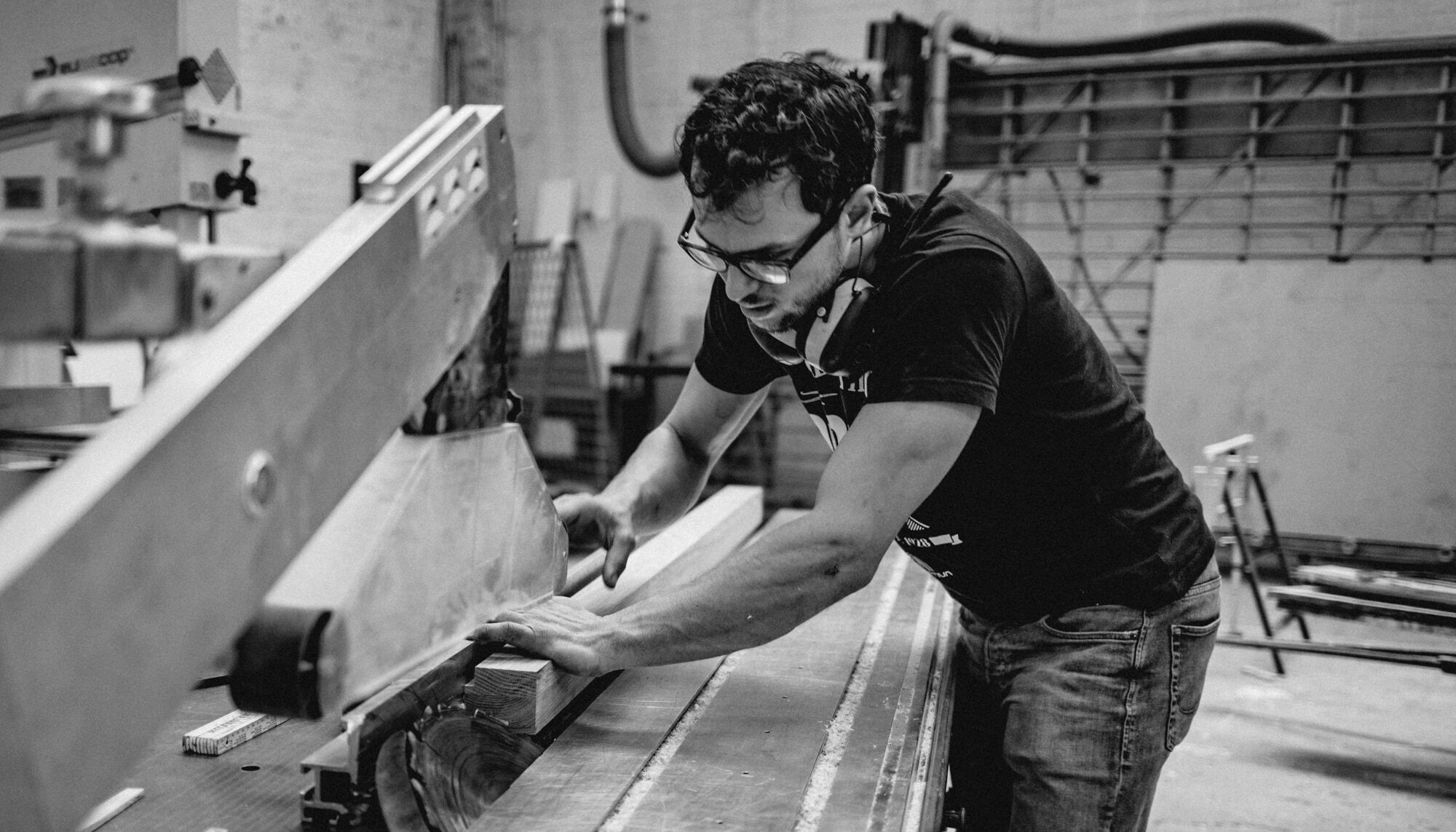 formstabil-bootsbau-möbelbau-flensburg-lucas30von92 - Deutsche Manufakturenstrasse Handwerker in einer Werkstatt schneidet Holz mit einer Tischsäge, um Möbel für den Bootsbau zu erstellen.