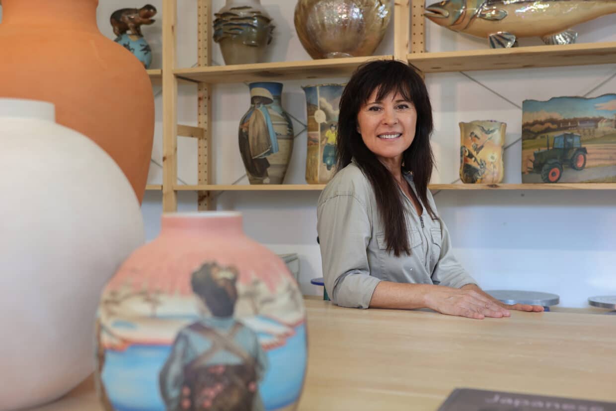 Victoria Tobostai lächelt in ihrem Atelier, umgeben von kunstvoll gestalteten Töpferwaren und Bildern.