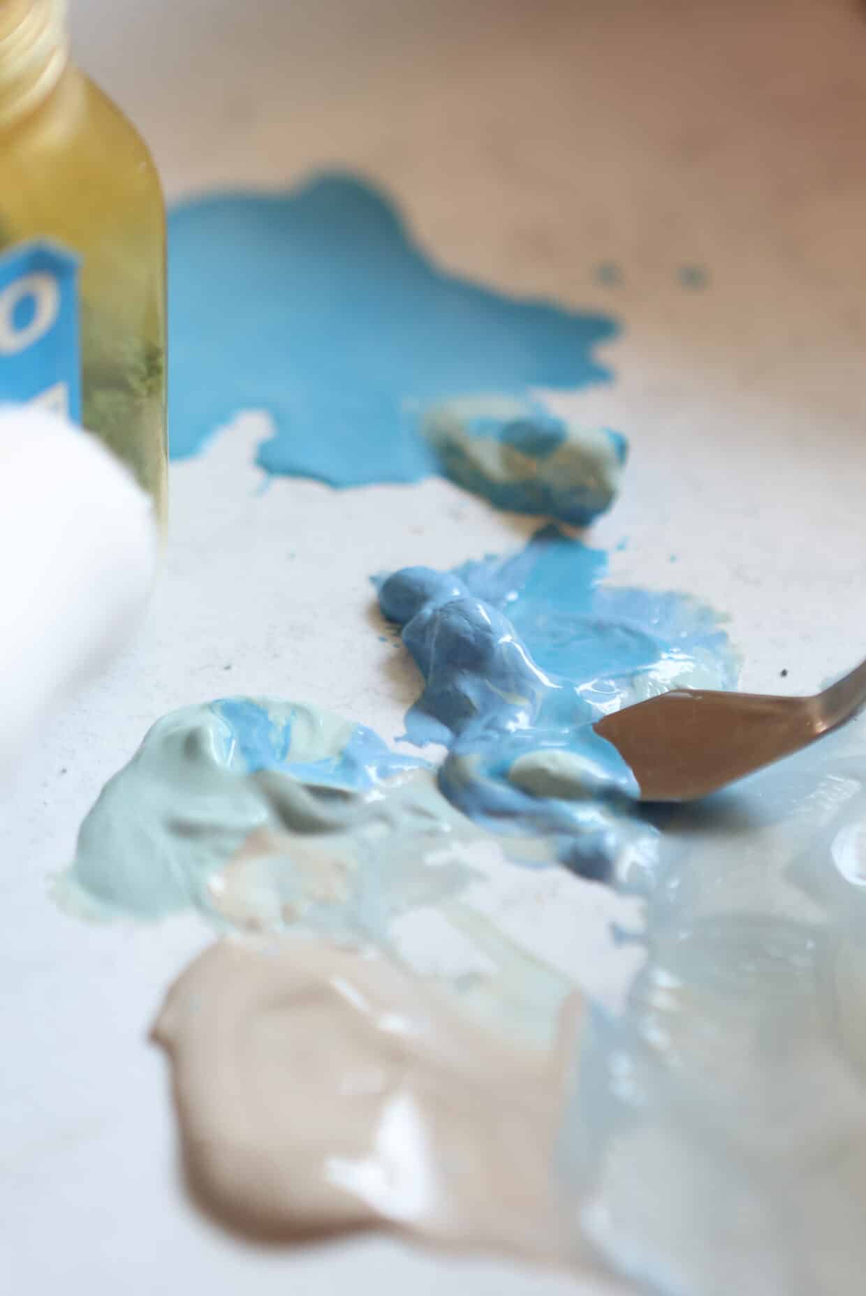 6_Victoria_Tobostai2025_069 - Deutsche Manufakturenstrasse Farbenfrohe Mischung aus verschiedenen Blautönen und Erdtönen auf einer Arbeitsfläche, neben einem Pinsel und einer Far...