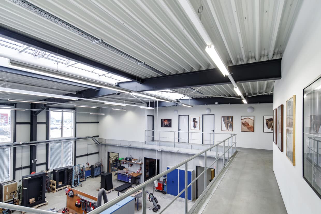 DOETTLING_Fertigung_I - Deutsche Manufakturenstrasse Luftaufnahme einer modernen Fertigungshalle mit Galerie, Kunstwerken an den Wänden und Arbeitsbereichen im Erdgeschoss.