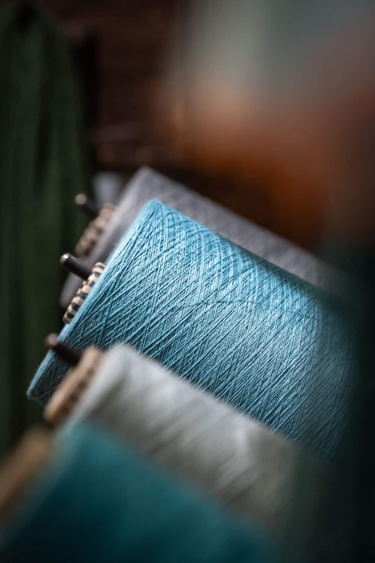 Garn blau grau Grieb U - Deutsche Manufakturenstrasse Drei Garnspulen in Blau- und Grautönen, mit Fokus auf der vordersten Spule in Türkis.