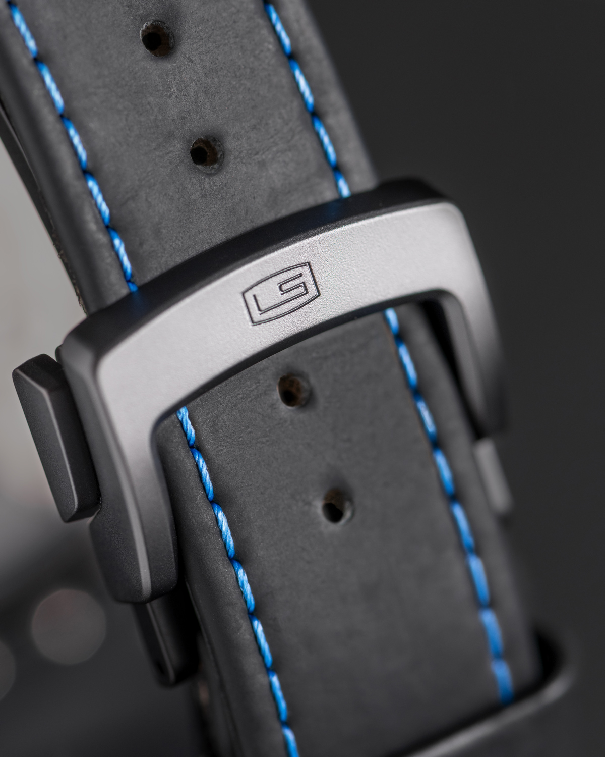 Lehmann-Kermaik-Band-RGB - Deutsche Manufakturenstrasse Schwarzes Armband mit blauen Nähten und einer silbernen Schnalle mit eingeprägtem Logo.