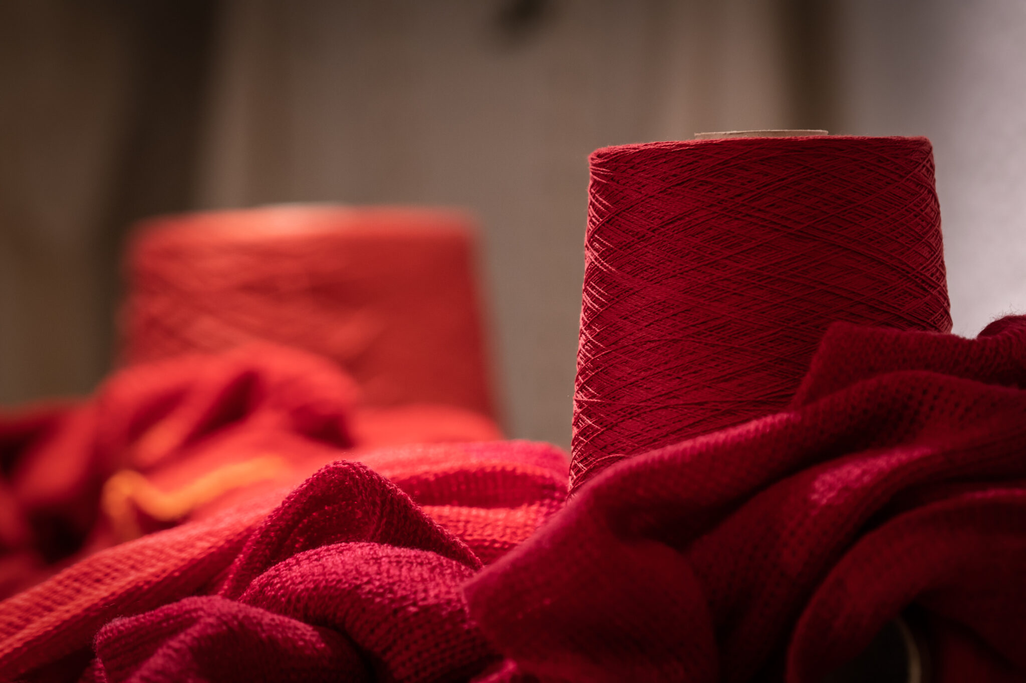 Merinowolle Grieb U - Deutsche Manufakturenstrasse Rote Merinowollknäuel und -stoffe, die in einem warmen Licht angeordnet sind.