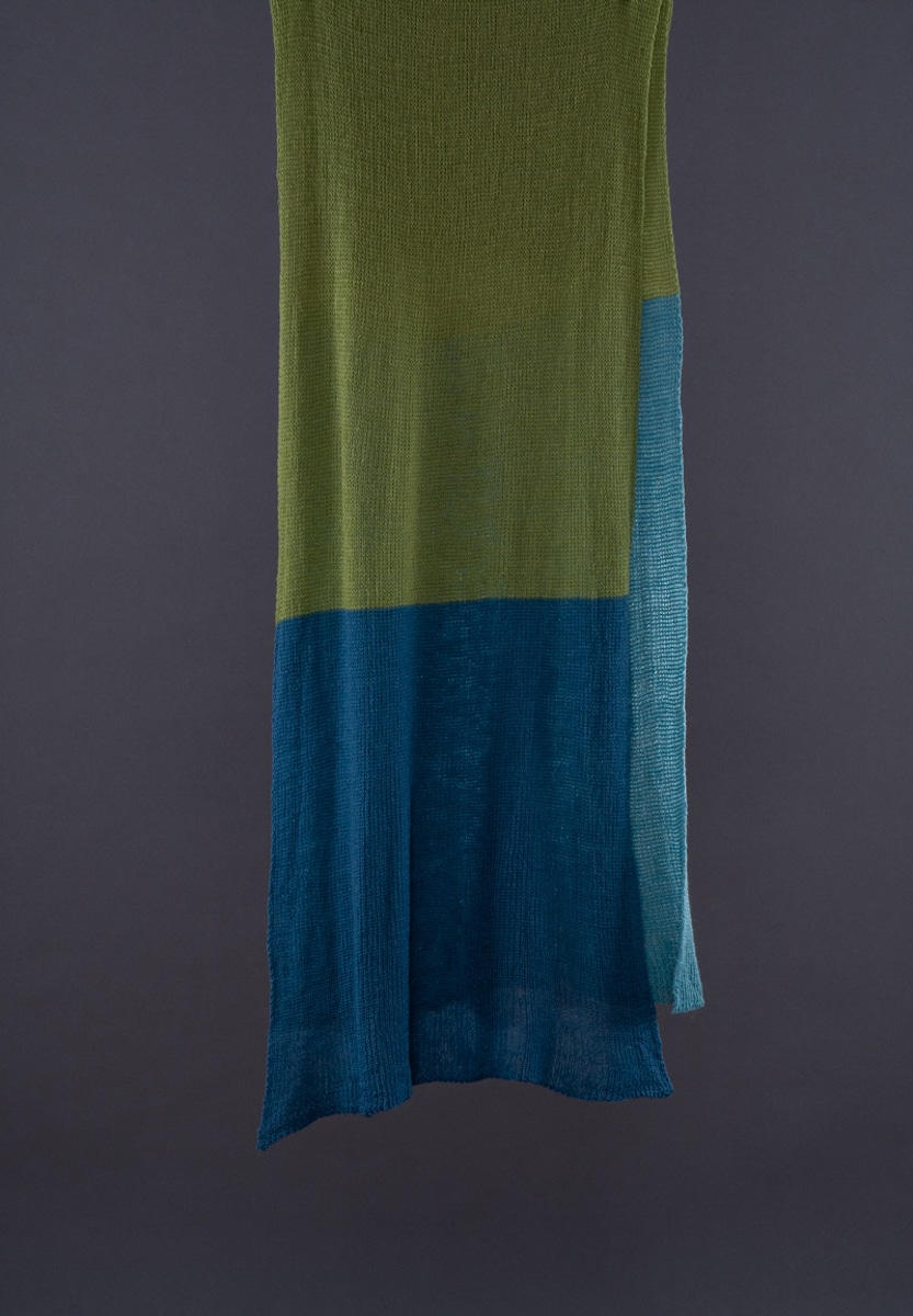 Schal grünblautürkis Merinowolle Grieb U - Deutsche Manufakturenstrasse Langer Schal in grün, blau und türkis aus Merinowolle, hängend vor dunklem Hintergrund.