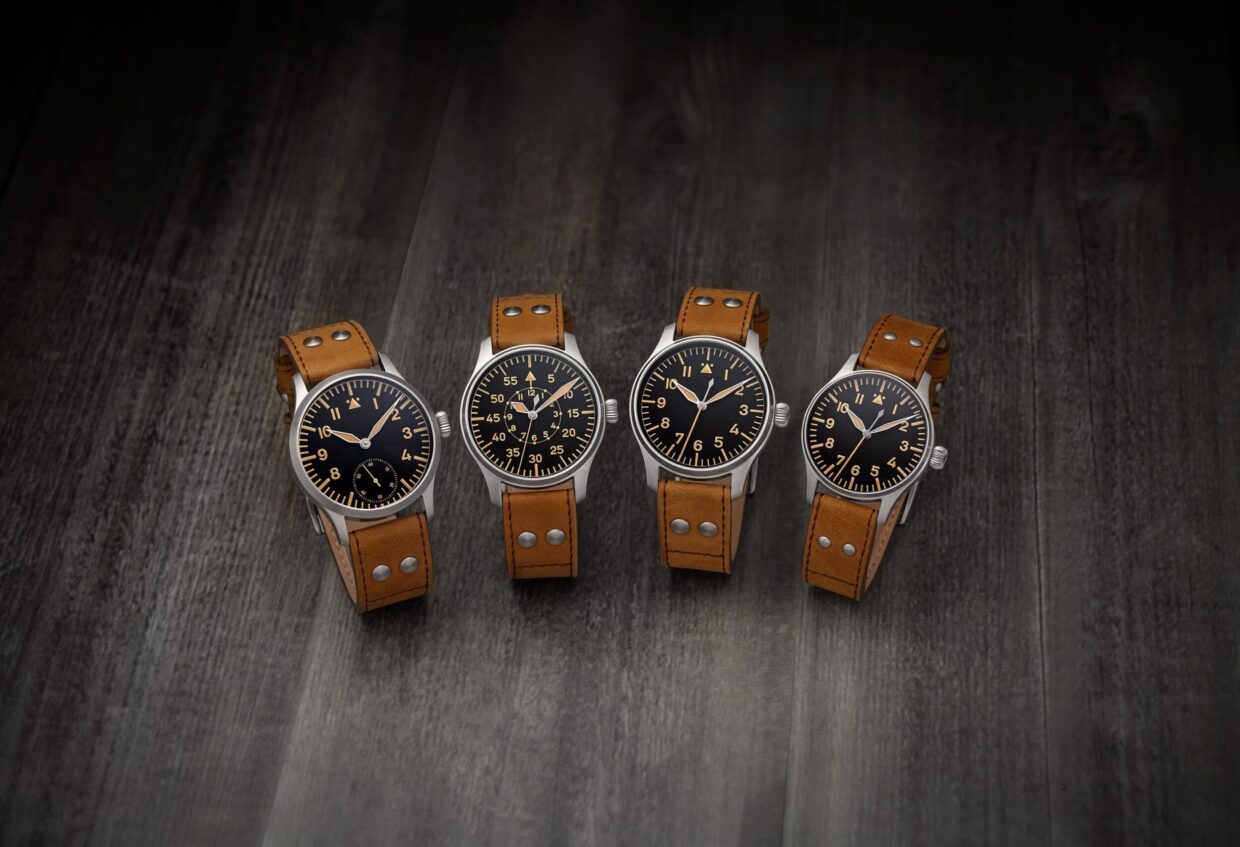 Flieger-Vintage-Gruppenbild-01-scaled - Deutsche Manufakturenstrasse Vier Vintage-Fliegeruhren mit schwarzen Zifferblättern und braunen Lederarmbändern auf einem dunklen Holzuntergrund.