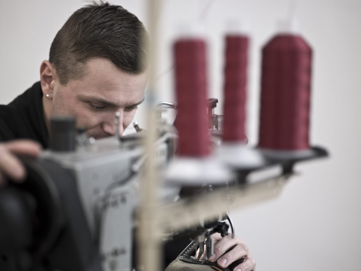 CF143910_xx - Deutsche Manufakturenstrasse Mann arbeitet konzentriert an einer Nähmaschine, rote Garnspulen im Hintergrund.