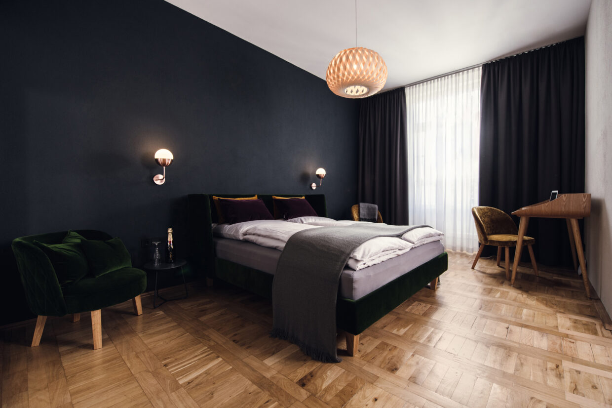 D85_8322 - Deutsche Manufakturenstrasse Modernes Schlafzimmer mit dunkler Wandfarbe, einem Bett mit grauer Bettwäsche, zwei Sessel und einem Schreibtisch.