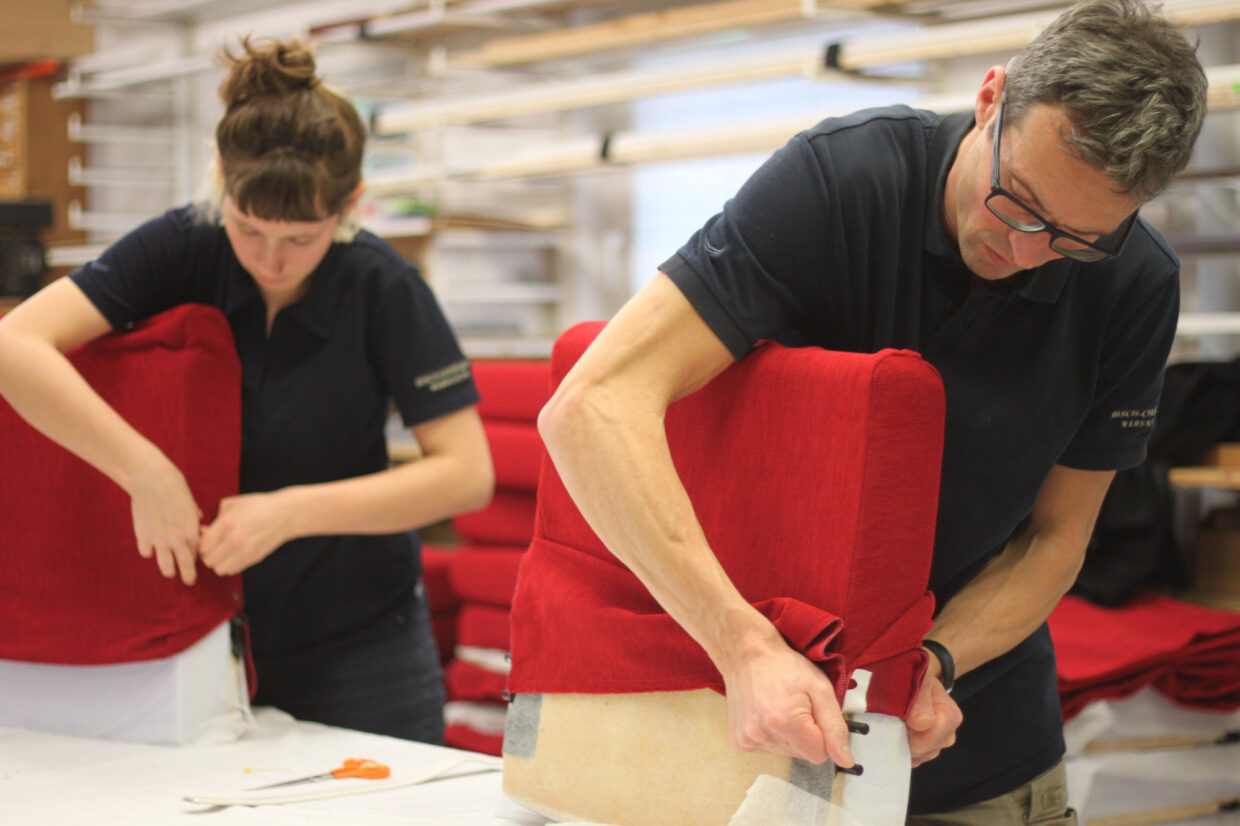 IMG_7675 - Deutsche Manufakturenstrasse Zwei Personen beziehen rote Polster in einer Werkstatt, während sie konzentriert an den Möbeln arbeiten.