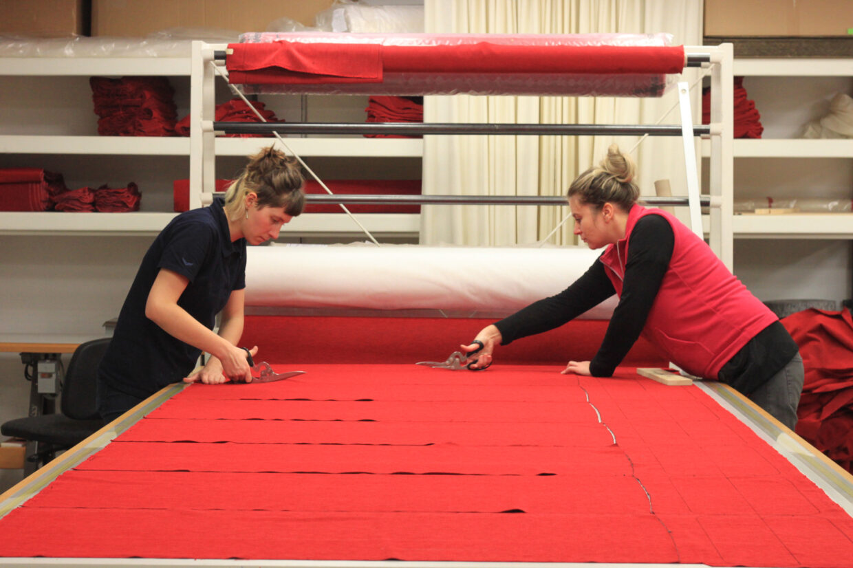 IMG_7835 - Deutsche Manufakturenstrasse Zwei Frauen schneiden roten Stoff auf einem Tisch in einer Werkstatt.