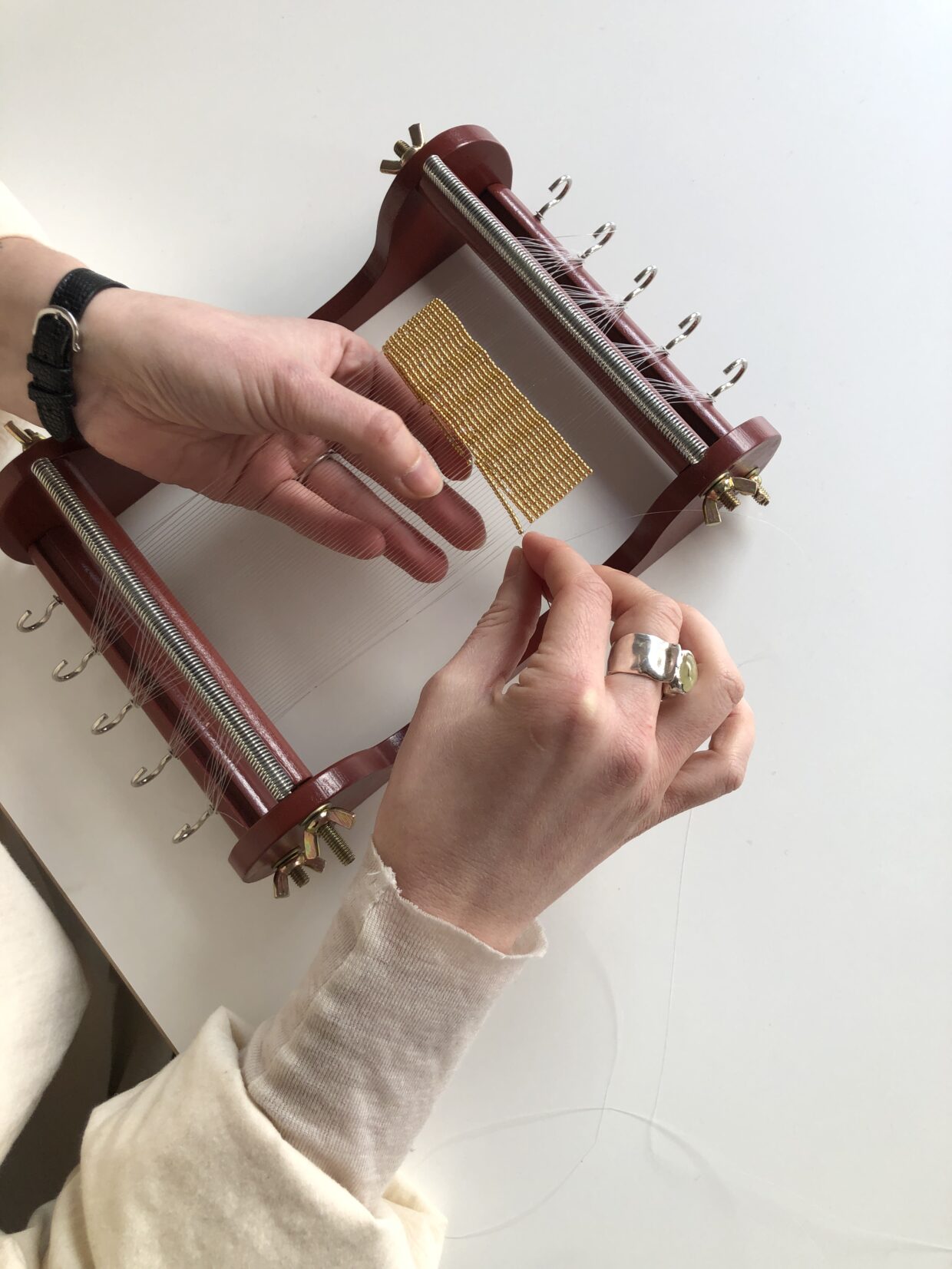 alinanaomi_bela25 - Deutsche Manufakturenstrasse Hände arbeiten an einem Webrahmen, um eine goldene Stoffbahn zu erstellen.