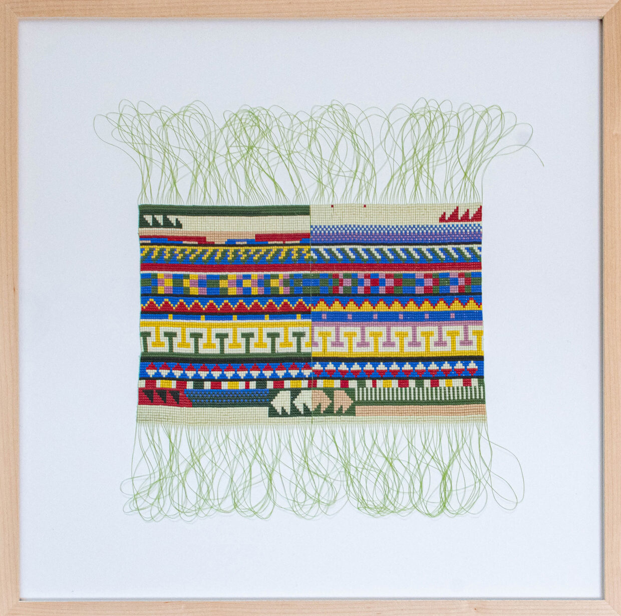 seminole_patchwork_II - Deutsche Manufakturenstrasse Buntes Seminole-Patchwork mit geometrischen Mustern und grünen Fäden, gerahmt in einem Holzrahmen.