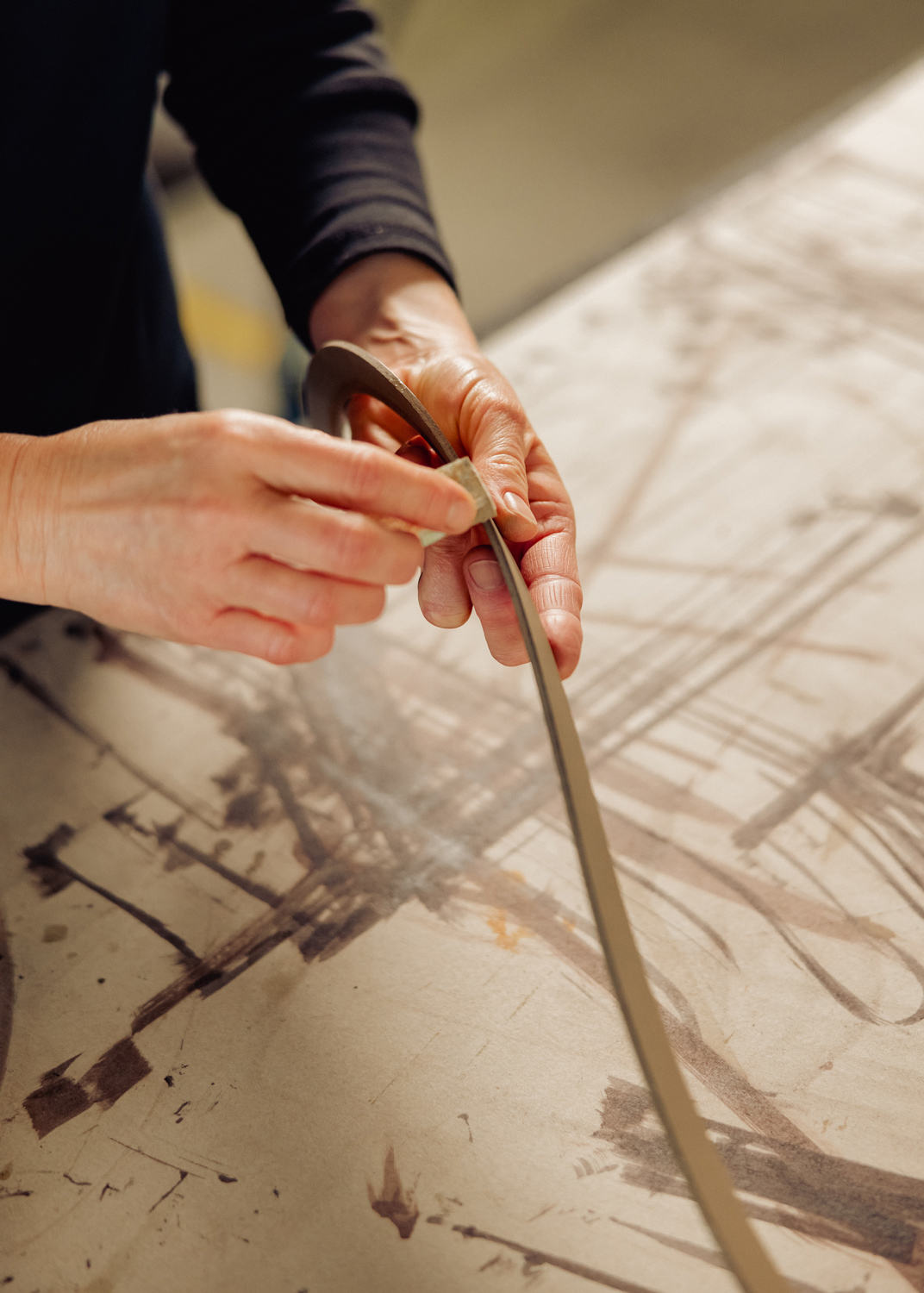 WEBFriends-of-Friends-Walter-Knoll-Shinzo-5581jpg_master - Deutsche Manufakturenstrasse Hände, die vorsichtig ein flexibles Material auf einer Tischoberfläche mit künstlerischen Strichen anbringen.