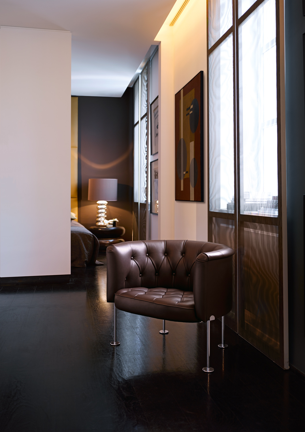 WEBWK-Haussmann_310-0018-H_master - Deutsche Manufakturenstrasse Brauner, gepolsterter Sessel mit modernen Beinen in einem eleganten Raum mit Kunstwerken und sanfter Beleuchtung.