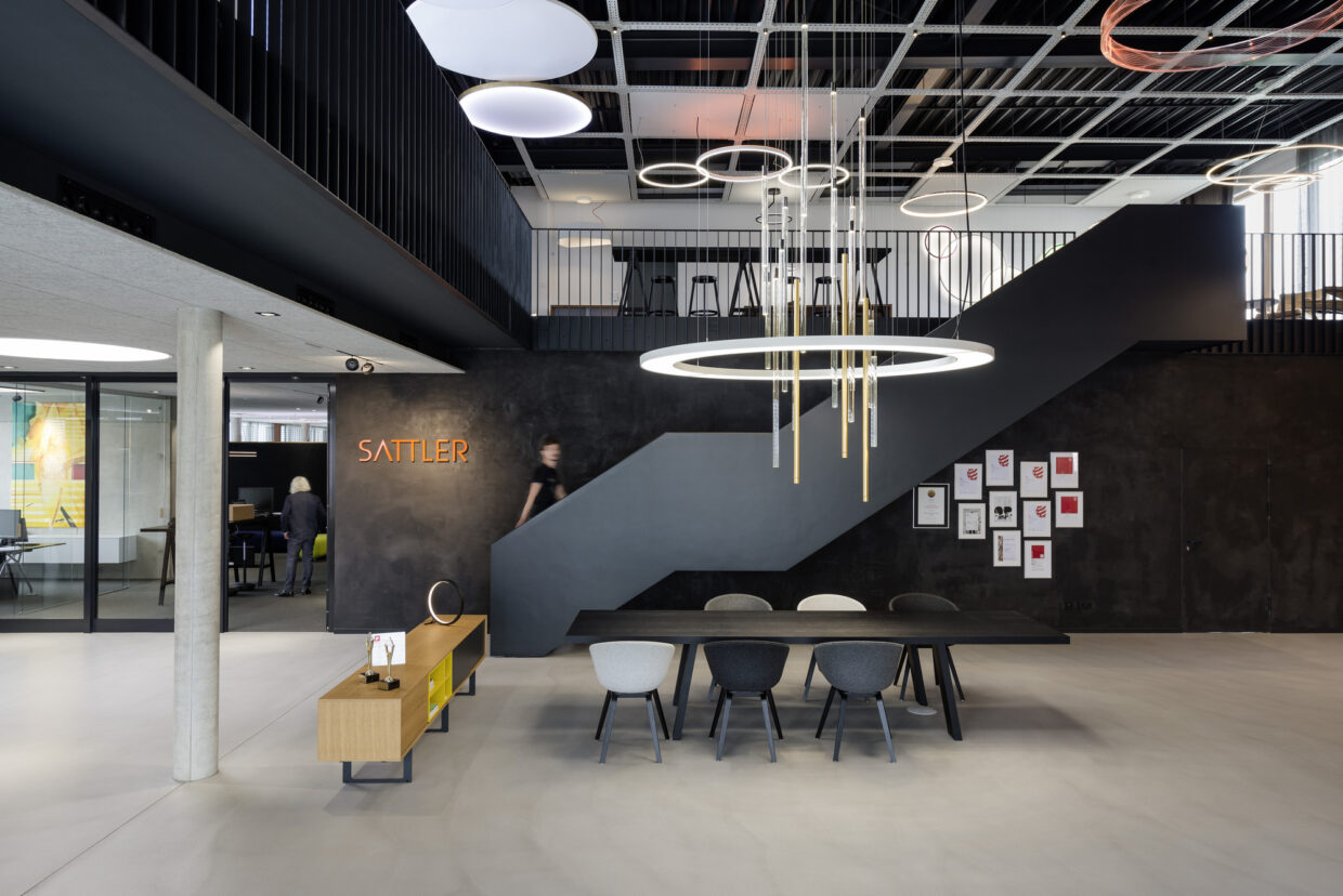 02_SATTLER_Firmensitz_Foyer_Foto Andreas Körner - Deutsche Manufakturenstrasse Modernes Foyer des Sattler Firmensitzes mit minimalistischer Einrichtung, großen Lampen und einer Treppe im Hintergrund.