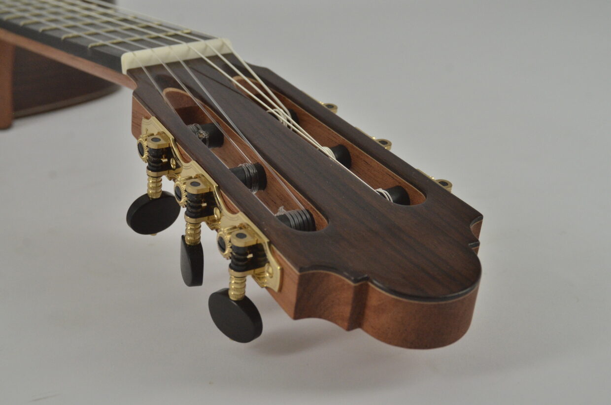 Detailaufnahme des Kopfes einer Gitarre mit Saiten und Mechaniken, aus Holz gefertigt.