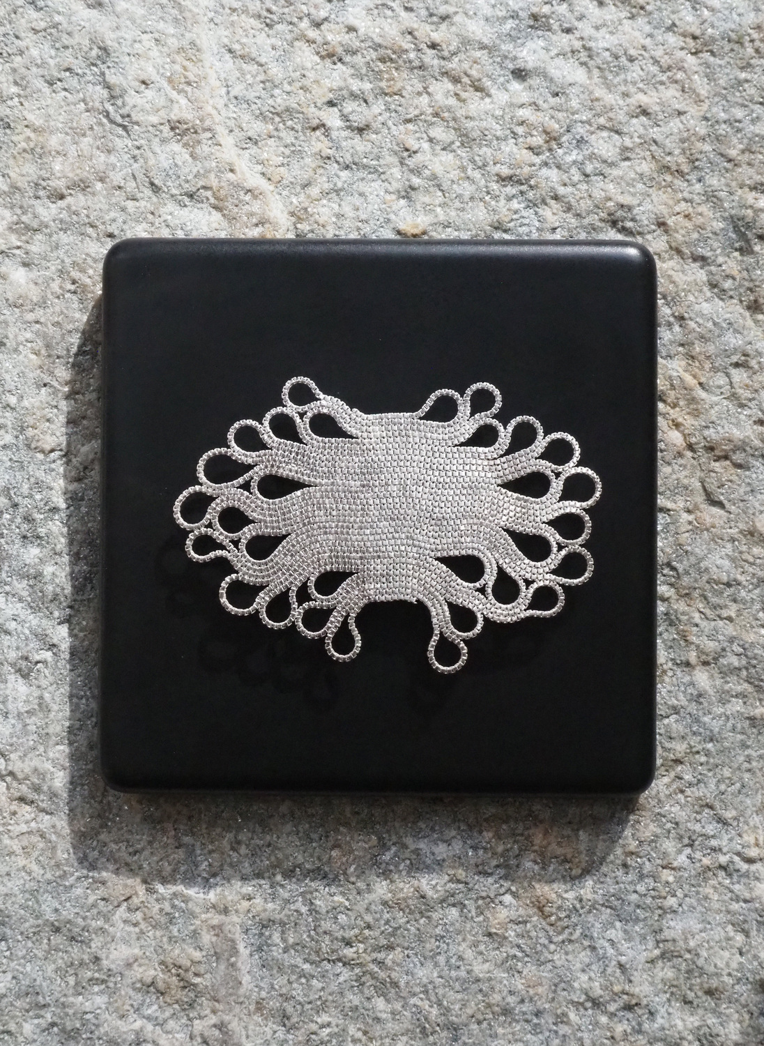 11 Brosche Display Kopie 1 - Deutsche Manufakturenstrasse Silberne Brosche mit filigranem, geschwungenem Design auf schwarzem Untergrund.