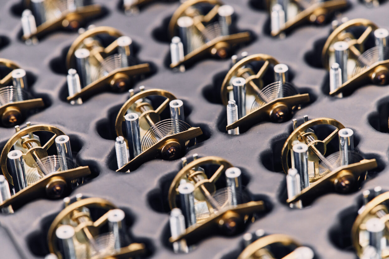 210121_Hermle_Corporate Shooting-244 1 - Deutsche Manufakturenstrasse Detailaufnahme von präzisen Uhrwerkkomponenten in einer strukturierten Anordnung auf einem dunklen Hintergrund.