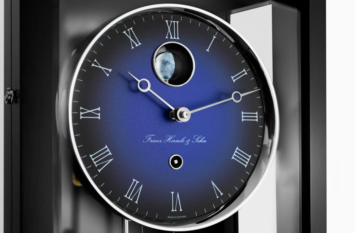 71013-740761_Detailaufnahme 1 - Deutsche Manufakturenstrasse Detailaufnahme einer Wanduhr mit blauem Ziffernblatt, römischen Ziffern und einem kleinen Mondfenster.