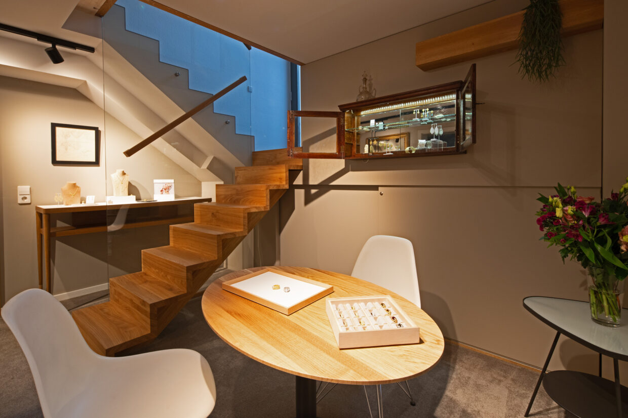 Atelier Adolph-021 1 - Deutsche Manufakturenstrasse Helles Atelier mit Holztreppe, runder Tisch, weißen Stühlen und Vitrine mit Schmuckstücken. Blumenarrangement auf dem T...