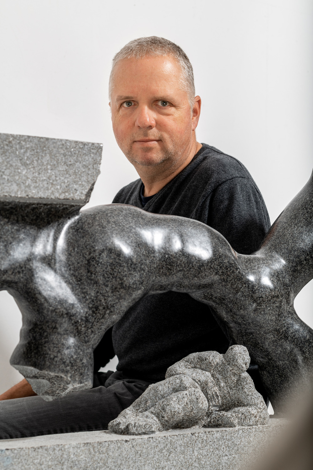 Christoph Traub 1 - Deutsche Manufakturenstrasse Mann mit kurzen grauen Haaren sitzt neben einer grauen Skulptur, die einen menschlichen Körper darstellt.